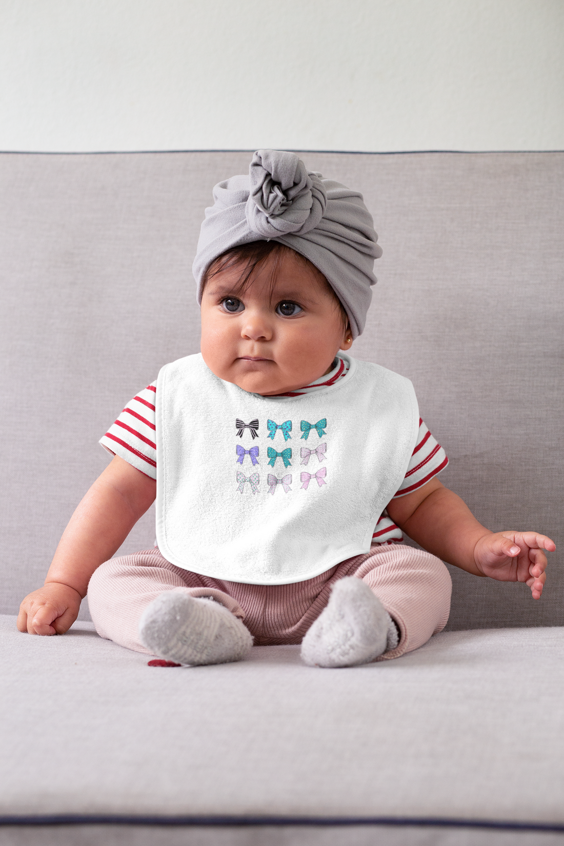 A close-up of a baby wearing a bib while sitting on a couch. The bib, part of FireBrook Designs' collection, embodies comfort and style for toddlers.