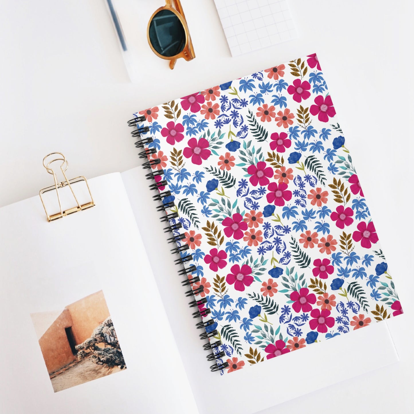 Spiral Notebook, Durable Cover, Ruled, 6x8, featuring a vibrant floral design, sits atop an open magazine, surrounded by a pen and sunglasses, embodying FireBrook Essentials' stylish and joyful approach to stationery.