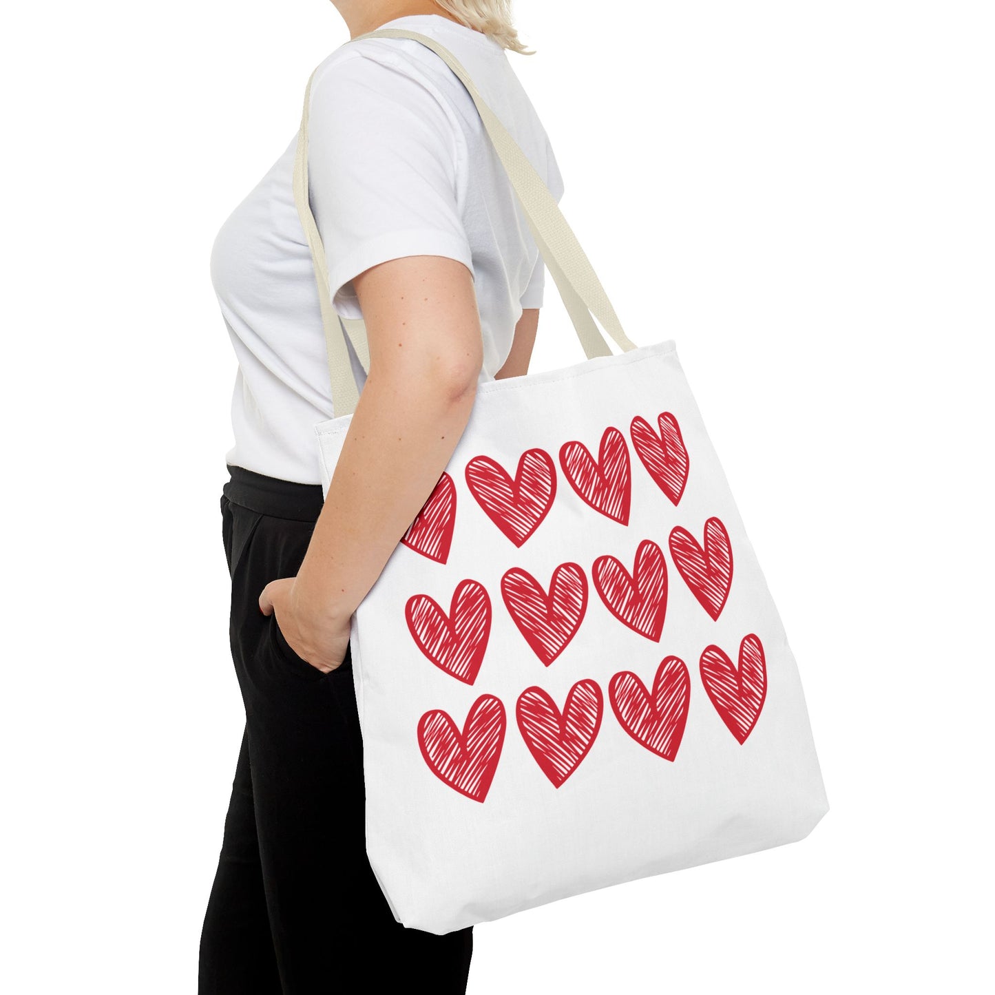 A woman holds the Hearts Tote Bag, featuring a white background adorned with red hearts. Ideal for adding charm to daily outfits, this FireBrook Designs accessory combines style with durability.