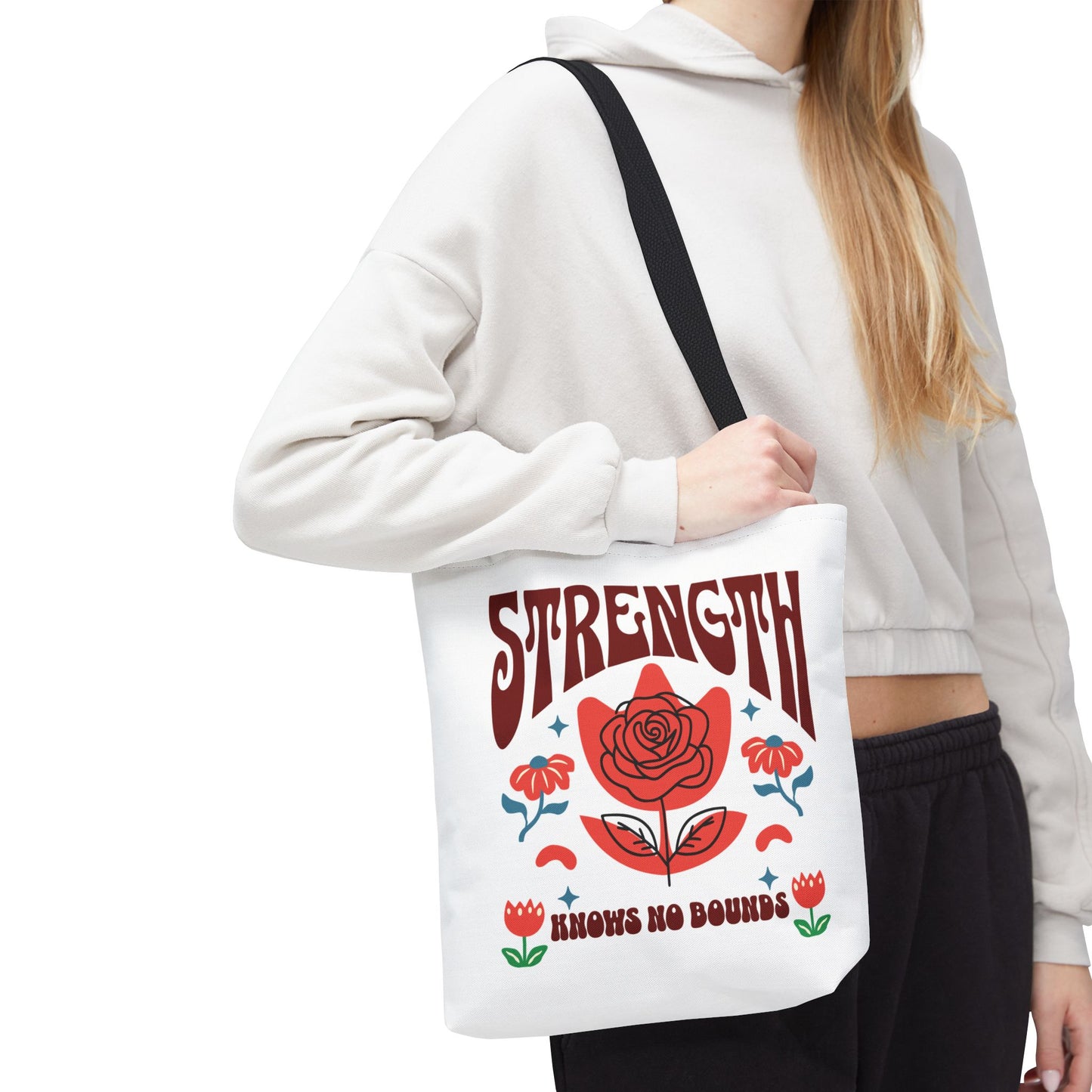 Woman holding the Strength Knows No Bounds Tote Bag, featuring a red rose design and quote. Ideal for everyday use and gifting, emphasizing strength and resilience.