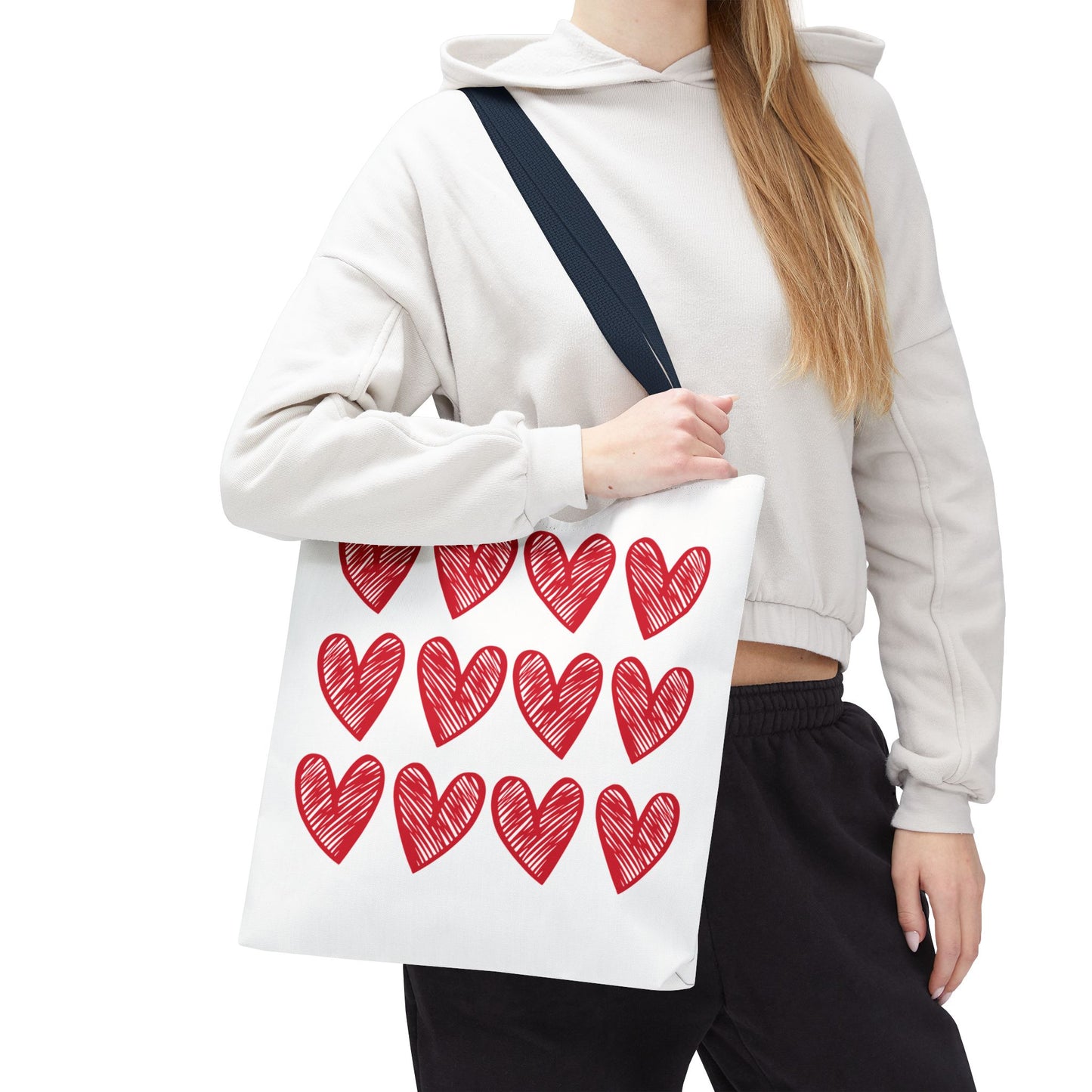 Hearts Tote Bag: A woman holds a charming white tote adorned with red hearts, showcasing its playful design. Perfect for adding a cheerful touch to any outfit, reflecting FireBrook Essentials' joyful style.
