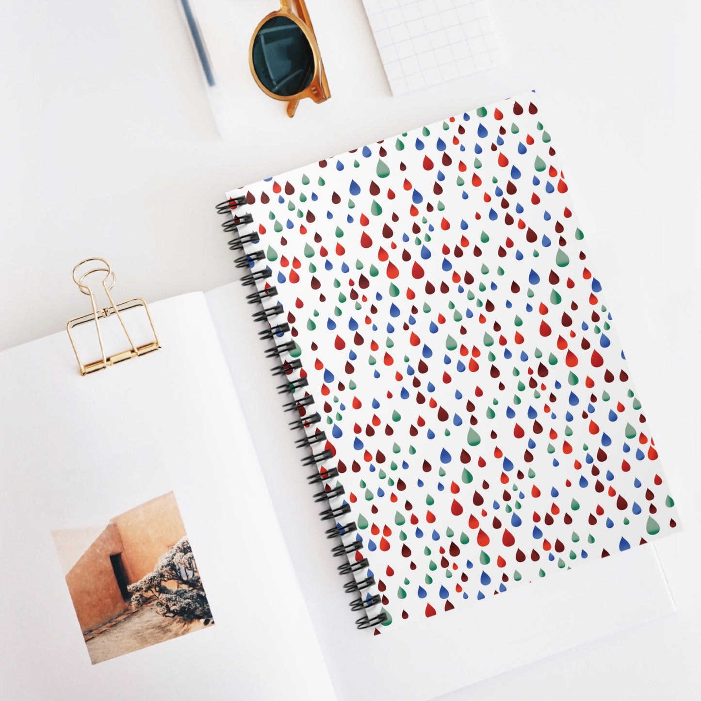 SPIRAL NOTEBOOK. DURABLE COVER, RULES, 6X8 - RAINDROPS features a vibrant teardrop pattern, ideal for stylish note-taking. Accompanied by minimal desktop accessories, showcasing its compact, eco-friendly design.