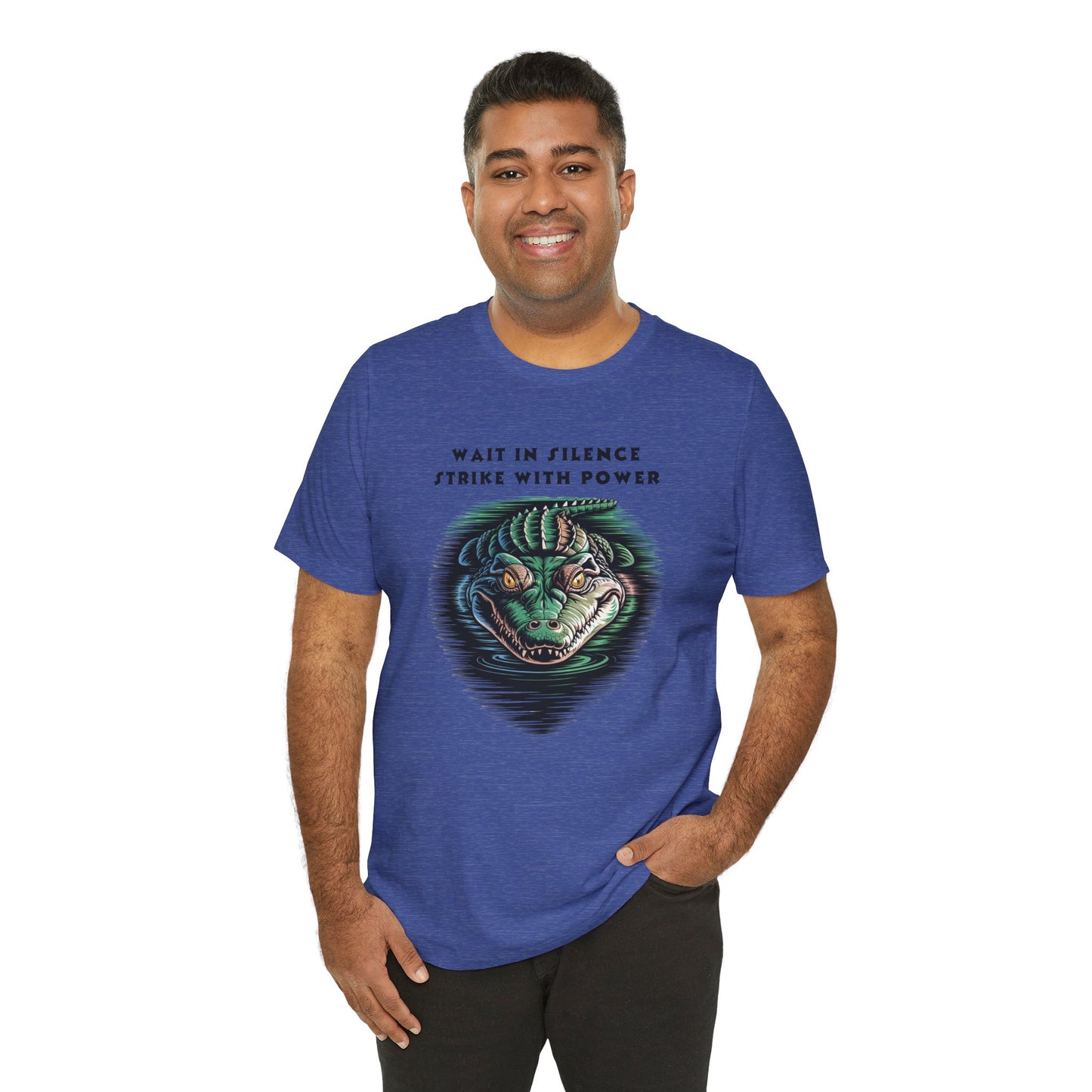Crocodile: Walk in Silence, Strike with Purpose Bella+Canvas Unisex T-Shirt features a man smiling in a blue tee with a unique crocodile design, hands in pockets, embodying quiet strength and determination.