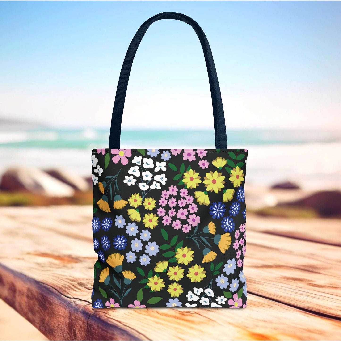 Starry Night Blooms Tote Bag on a wooden surface, featuring a vibrant, scattered floral pattern with clusters of blossoms and green leaves. Ideal for summer outings and designed for style and durability.