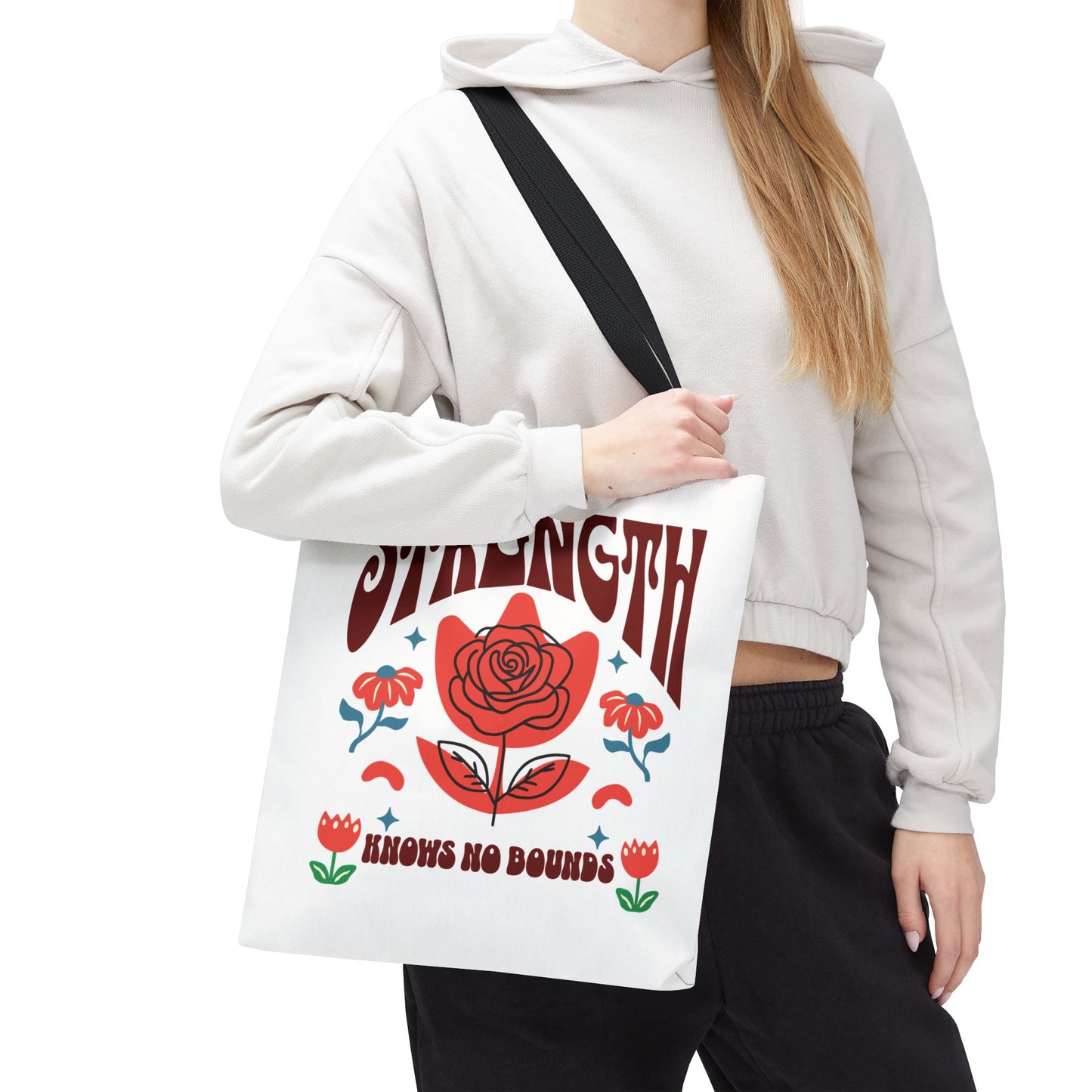 Woman holding the Strength Knows No Bounds Tote Bag, showcasing its durable design with black straps and a red rose detail. Ideal for everyday use.