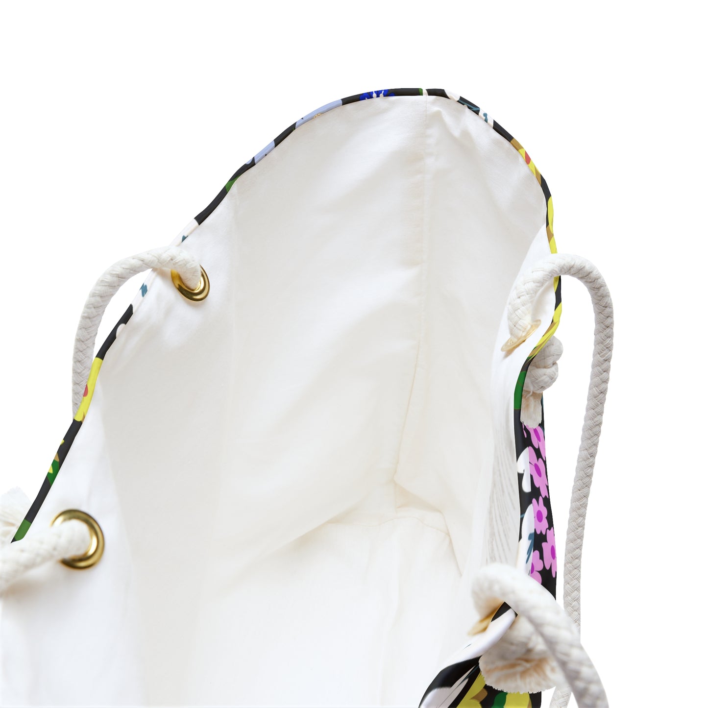 Weekender Bag with a cream-lined interior and braided rope handles through brass grommets, showcasing a hint of colorful floral print at the top edge, perfect for stylish travel.