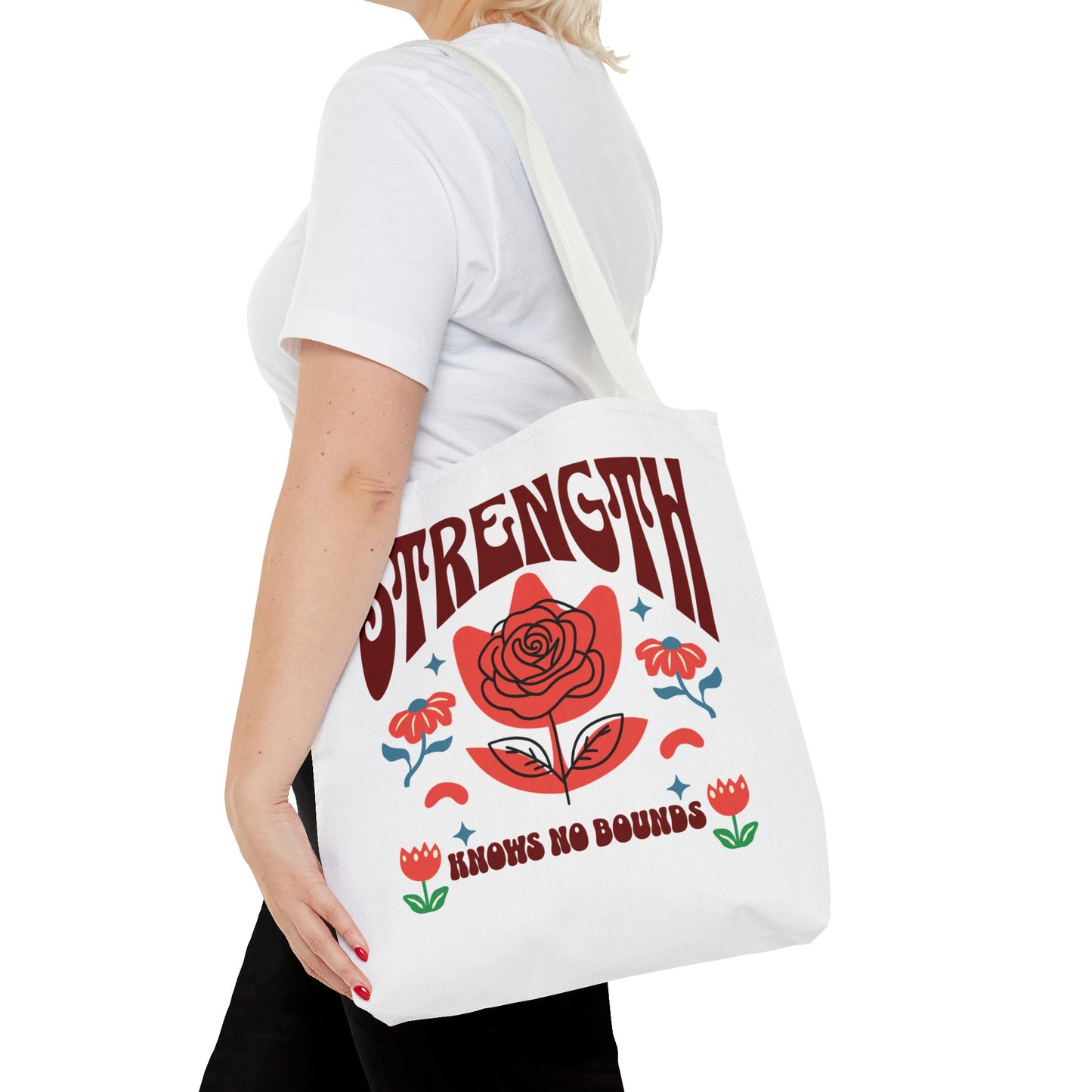 Strength Knows No Bounds Tote Bag, held by a woman, featuring a red rose design and text, ideal for everyday use with durable construction.