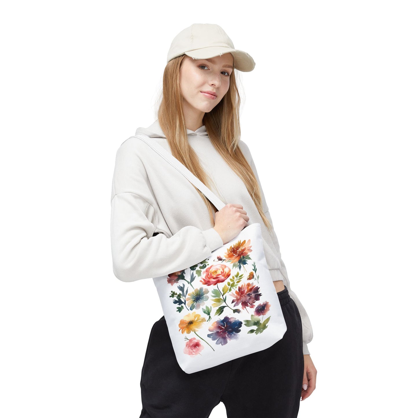 Woman wearing a hat and white sweatshirt holding a Watercolor Floral Tote Bag, showcasing its stylish design and practicality for daily use.