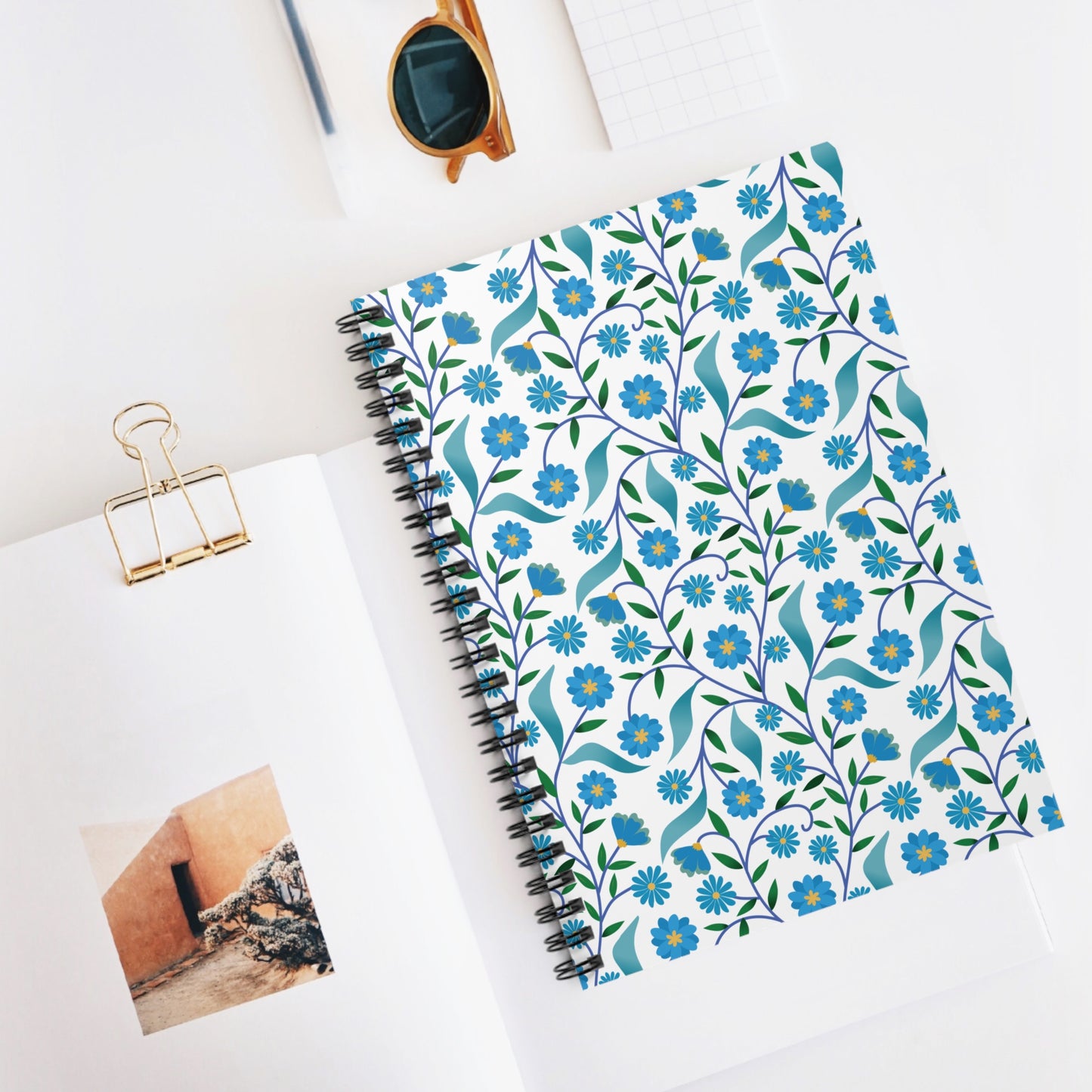 Spiral Notebook, Durable Cover, Rules, 6x8 - Blue Daisy Vine, featured in a minimalist workspace with stylish sunglasses and an open magazine, highlighting its elegant floral design and compact size.