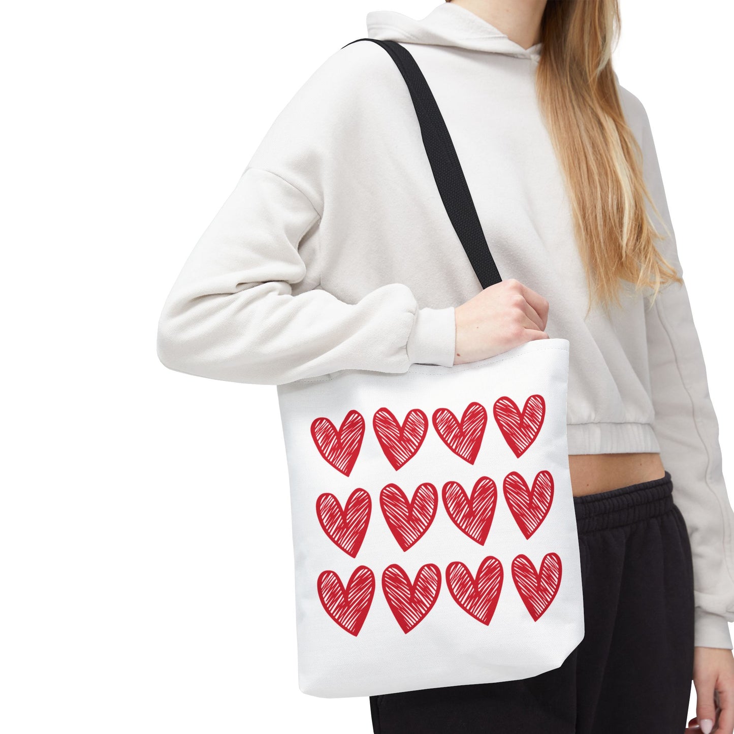 A woman holds the Hearts Tote Bag, a white bag adorned with red heart patterns, embodying FireBrook Designs' joyful and stylish essence, perfect for adding love to any outfit.