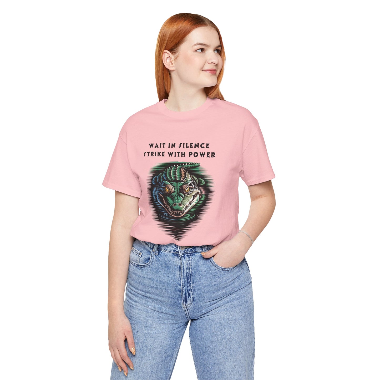 Crocodile: Walk in Silence, Strike with Purpose Bella+Canvas Unisex T-Shirt featuring a woman in a pink shirt and jeans, posing with a detailed crocodile design, reflecting bold, unique style.