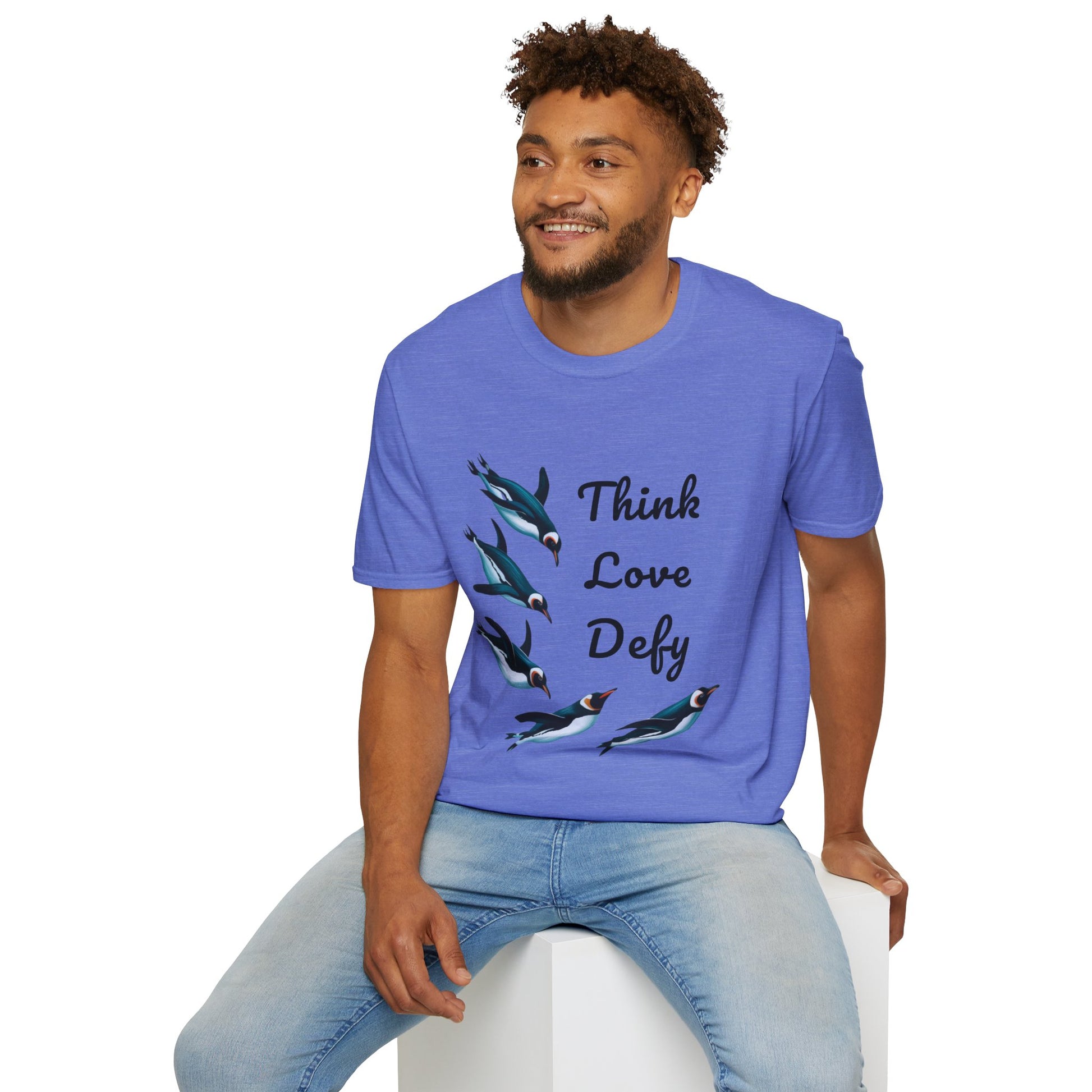 Think Love Defy Penguin Animal Nature Gildan Unisex T-Shirt featuring penguin design; a man models it while seated on a cube, showcasing its casual fit and comfort for nature enthusiasts.