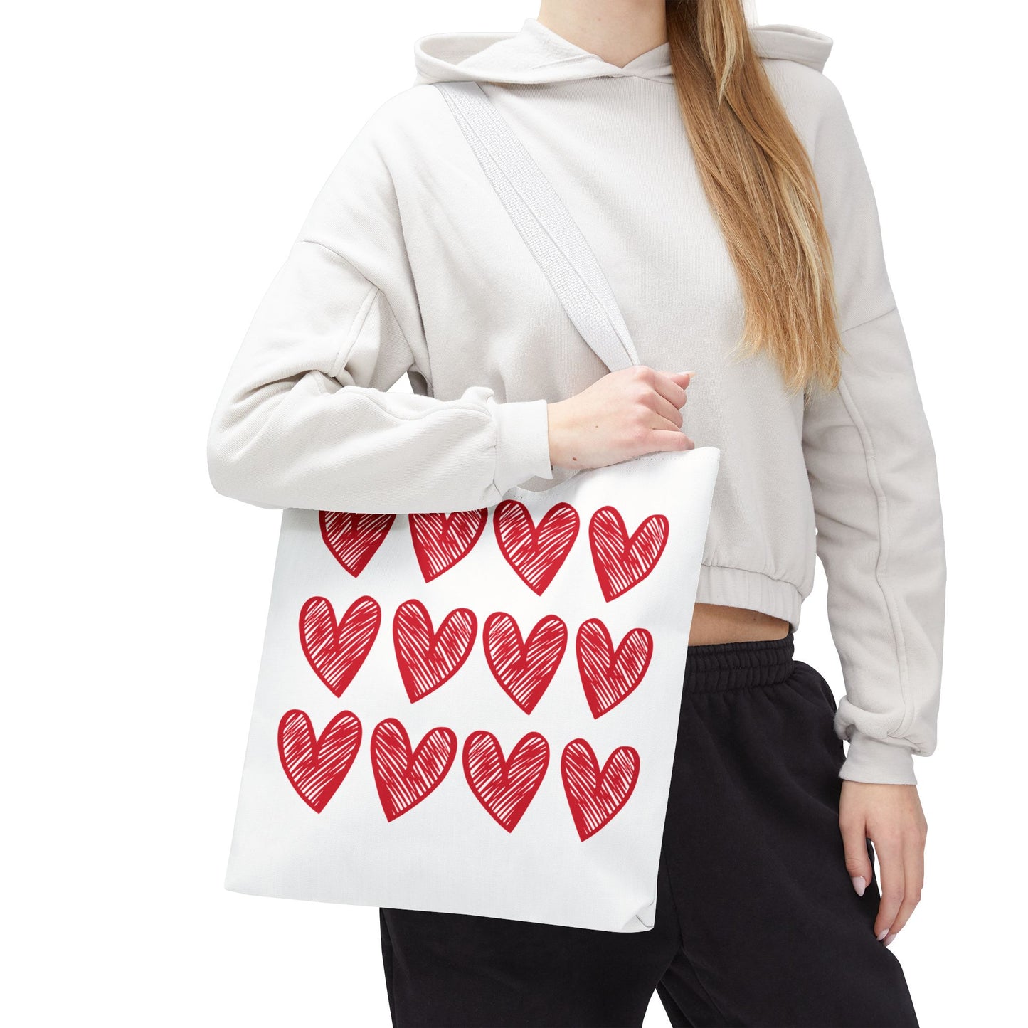 Hearts Tote Bag: A woman holds a stylish white tote bag adorned with red hearts, perfect for adding charm to everyday outfits, embodying FireBrook Essentials' uplifting and joyful design philosophy.