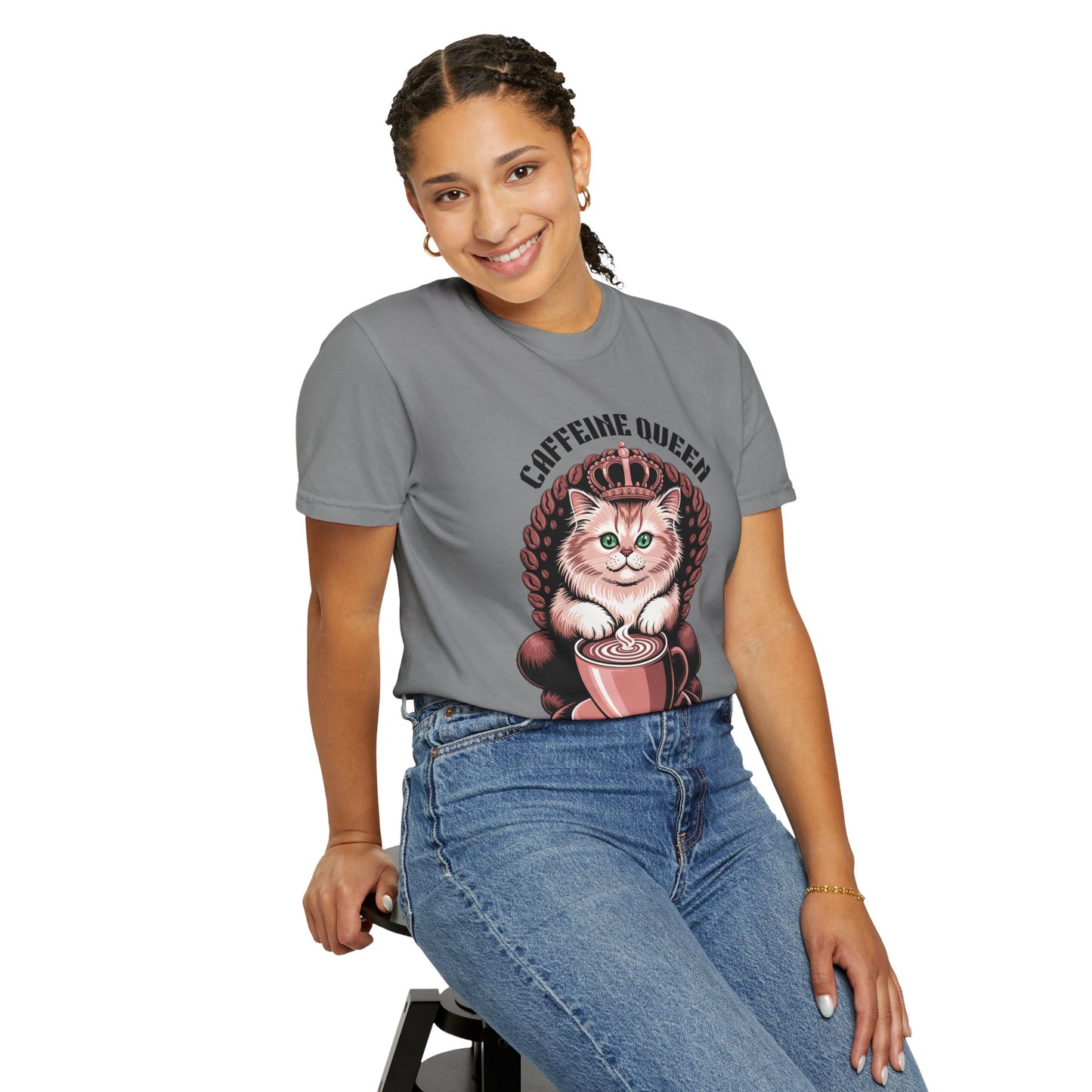 Cat Caffeine Queen T-shirt showcased by a smiling woman sitting on a stool. The shirt features a fun, playful design with a cat wearing a crown, ideal for cat and coffee enthusiasts.