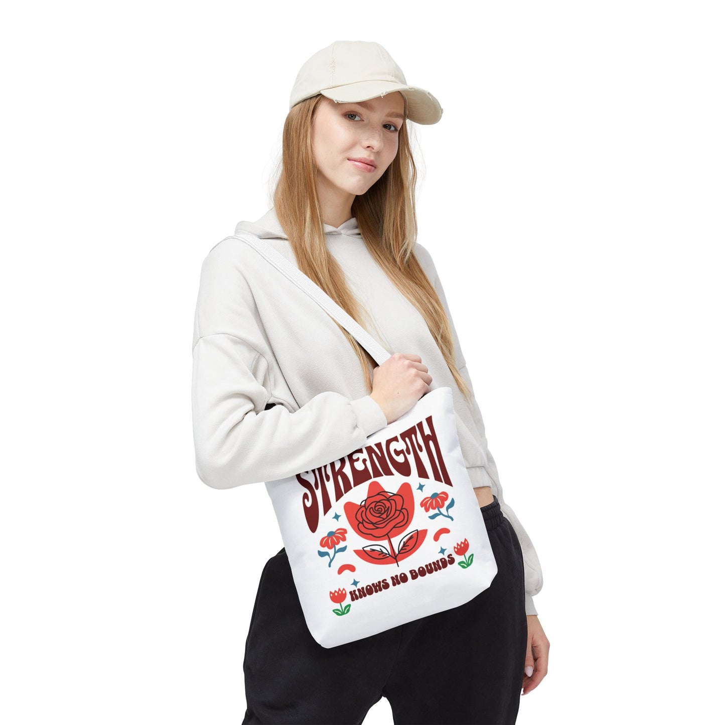 Woman in white hoodie holds Strength Knows No Bounds tote bag with red floral design, showcasing durability and style from FireBrook Essentials.