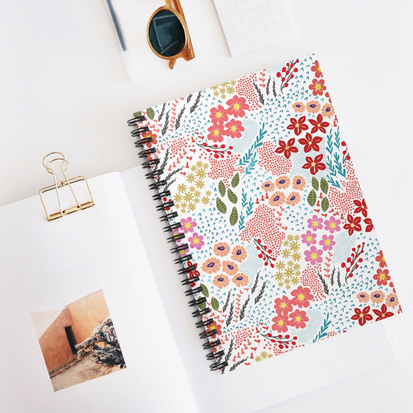 Floral Spiral Notebook with vibrant hand-drawn blooms, central on a white desk, exudes creativity and organization. Ideal for jotting, sketching, or journaling, it embodies FireBrook Designs' joyful, uplifting ethos.
