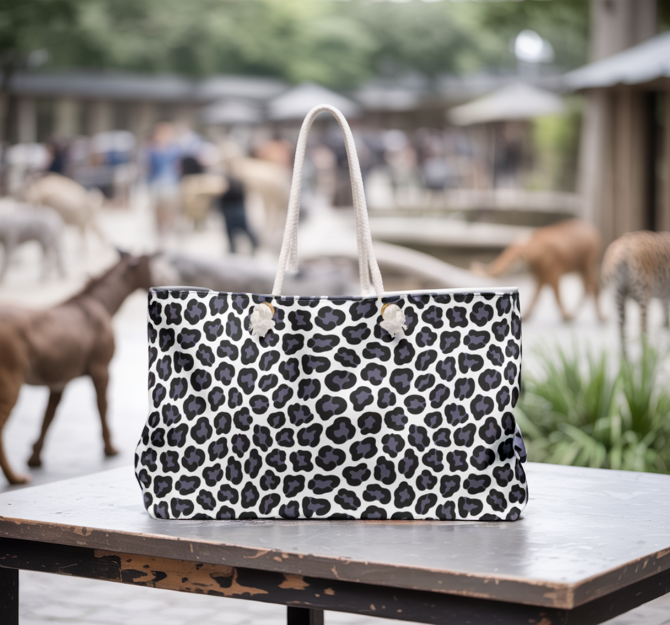 Weekender Bag - Gray Cheetah Print Duffle Bag on a table, showcasing its durable spun polyester fabric and stylish cheetah pattern. Features rope handles for easy carrying, embodying FireBrook Essentials' commitment to stylish, joyful travel accessories.