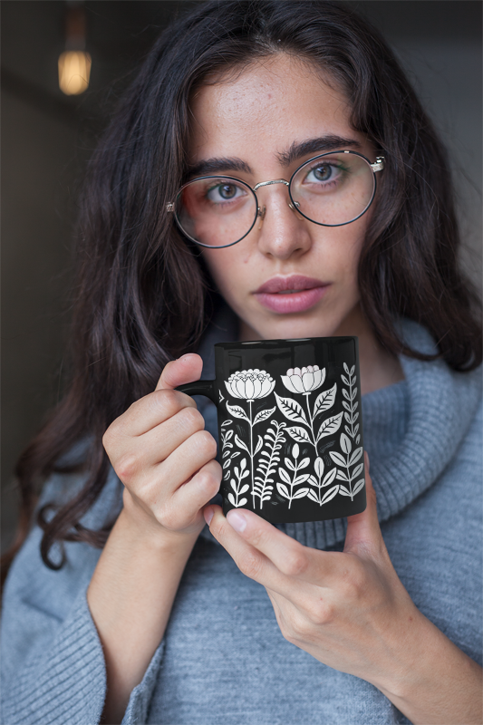 Vintage Flower Mug (11oz, 15oz) held by a person; features a minimalist black ceramic design with elegant white flowers, embodying FireBrook Designs' joyful, stylish essence for cozy coffee or tea moments.