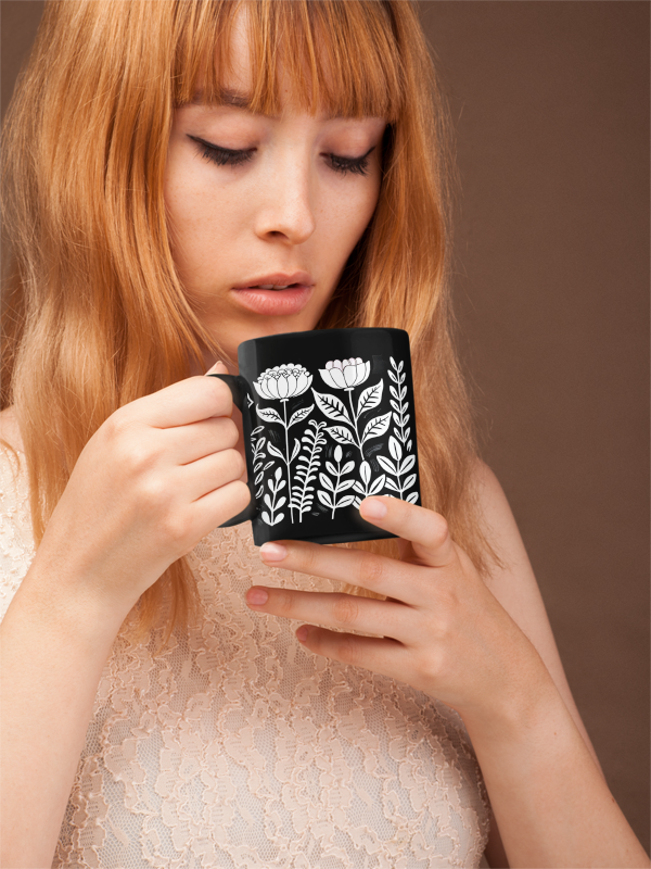 Vintage Flower Mug (11oz, 15oz): A woman holds a sleek black ceramic mug adorned with floral patterns, embodying minimalist elegance. Ideal for cozy drinks, it features a glossy finish, perfect for joyful gifting occasions.