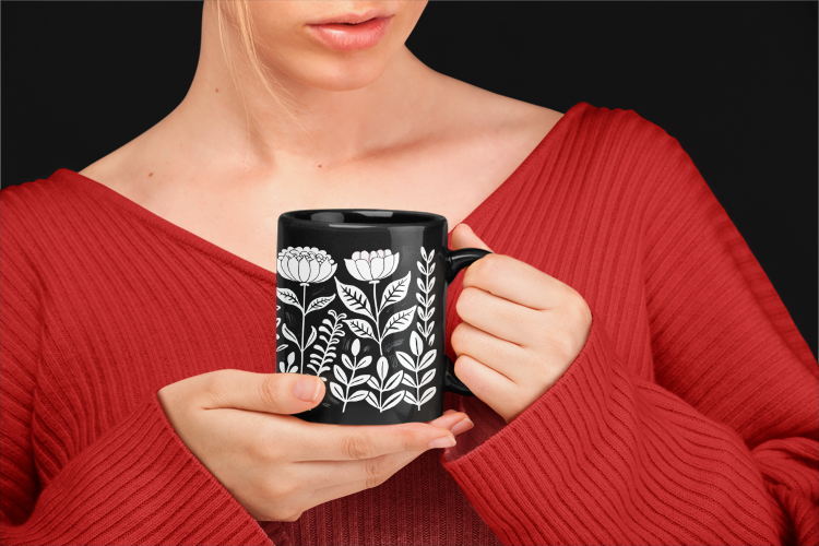 Vintage Flower Mug (11oz, 15oz) held by a woman, showcasing its elegant black ceramic design adorned with floral patterns, embodying minimalist aesthetics. Ideal for cozy mornings and gift occasions, from FireBrook Designs.