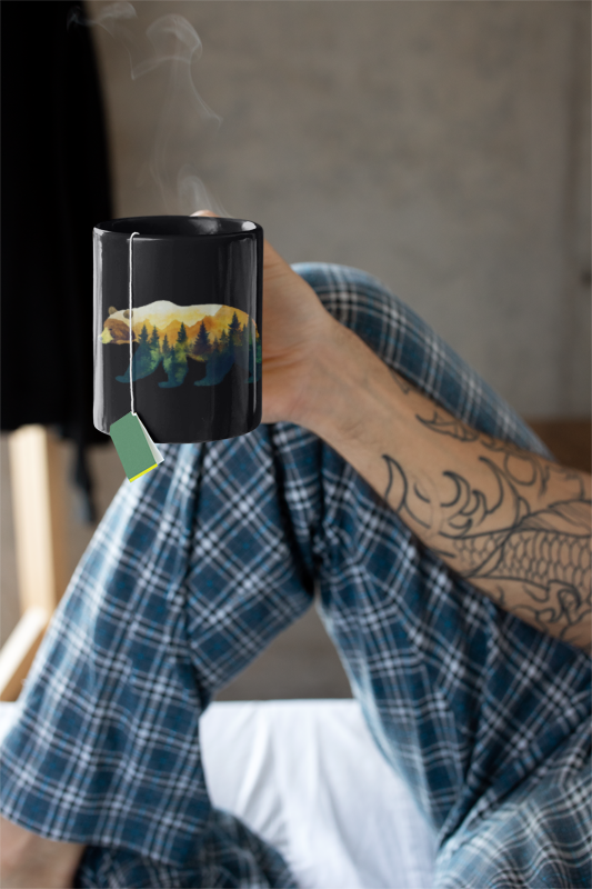 Bear in the Woods Mountain Mug (11 oz, 15 oz) held by a person, showcasing a bear and tree design, ideal for nature lovers. The mug’s rustic theme aligns with FireBrook Essentials' uplifting, nature-inspired products.