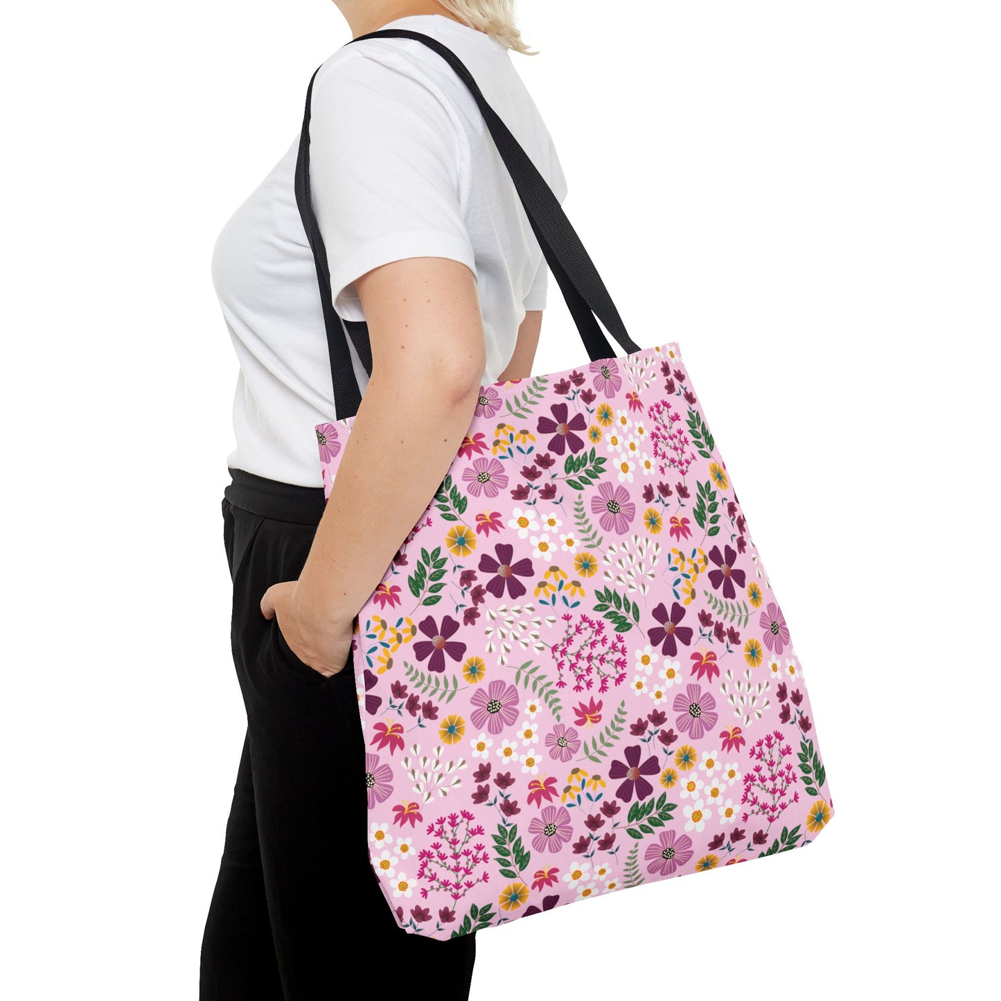 A person carries the Rose Garden Blush Tote Bag, showcasing its vibrant floral print and black straps. The tote is designed for durability and style, ideal for daily use with its spacious, reinforced structure.