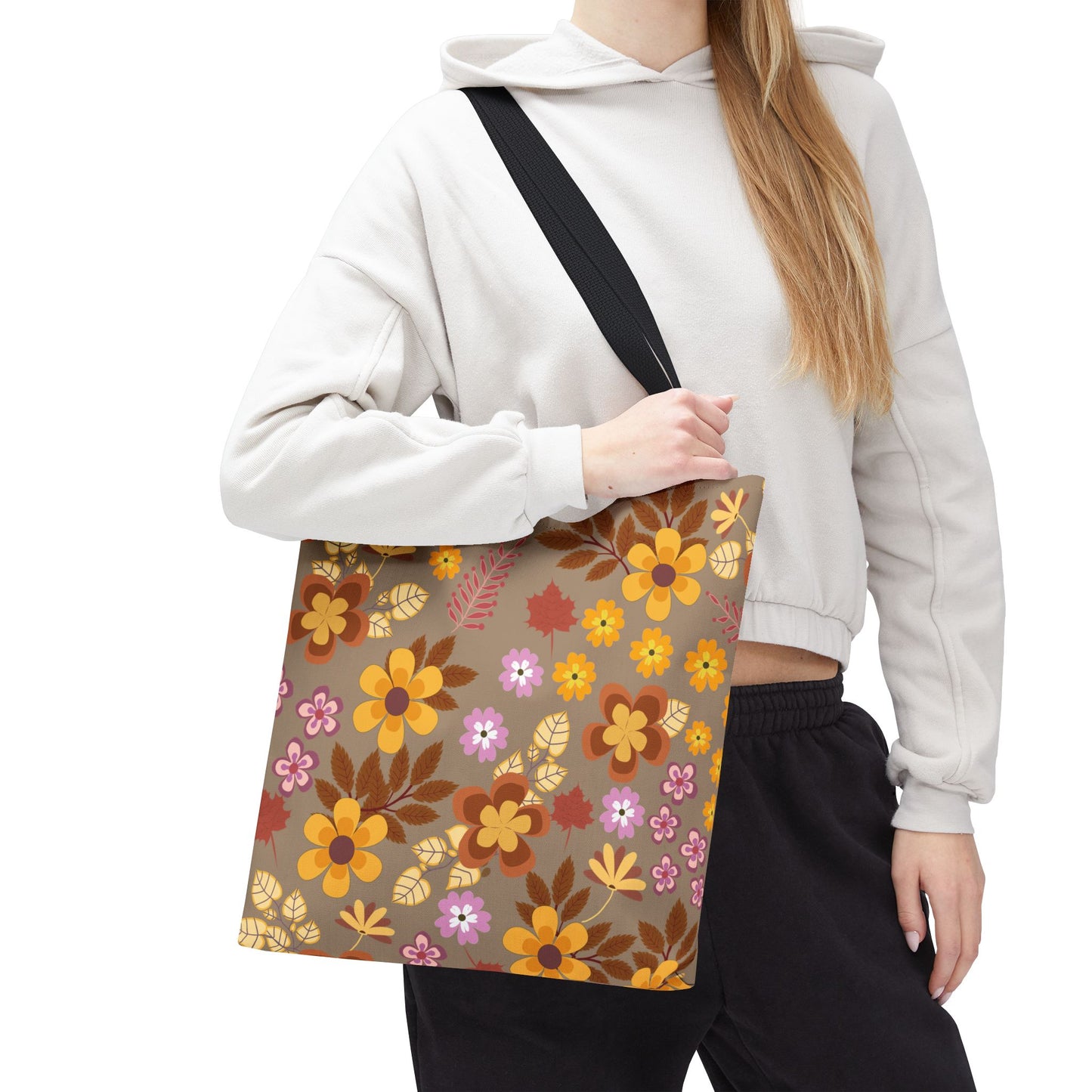 Person wearing light hoodie and dark pants holding the Harvest Brown Bloom Tote Bag, featuring retro floral print in vibrant yellows, oranges, and pinks, ideal for cheerful summer outings or beach trips.