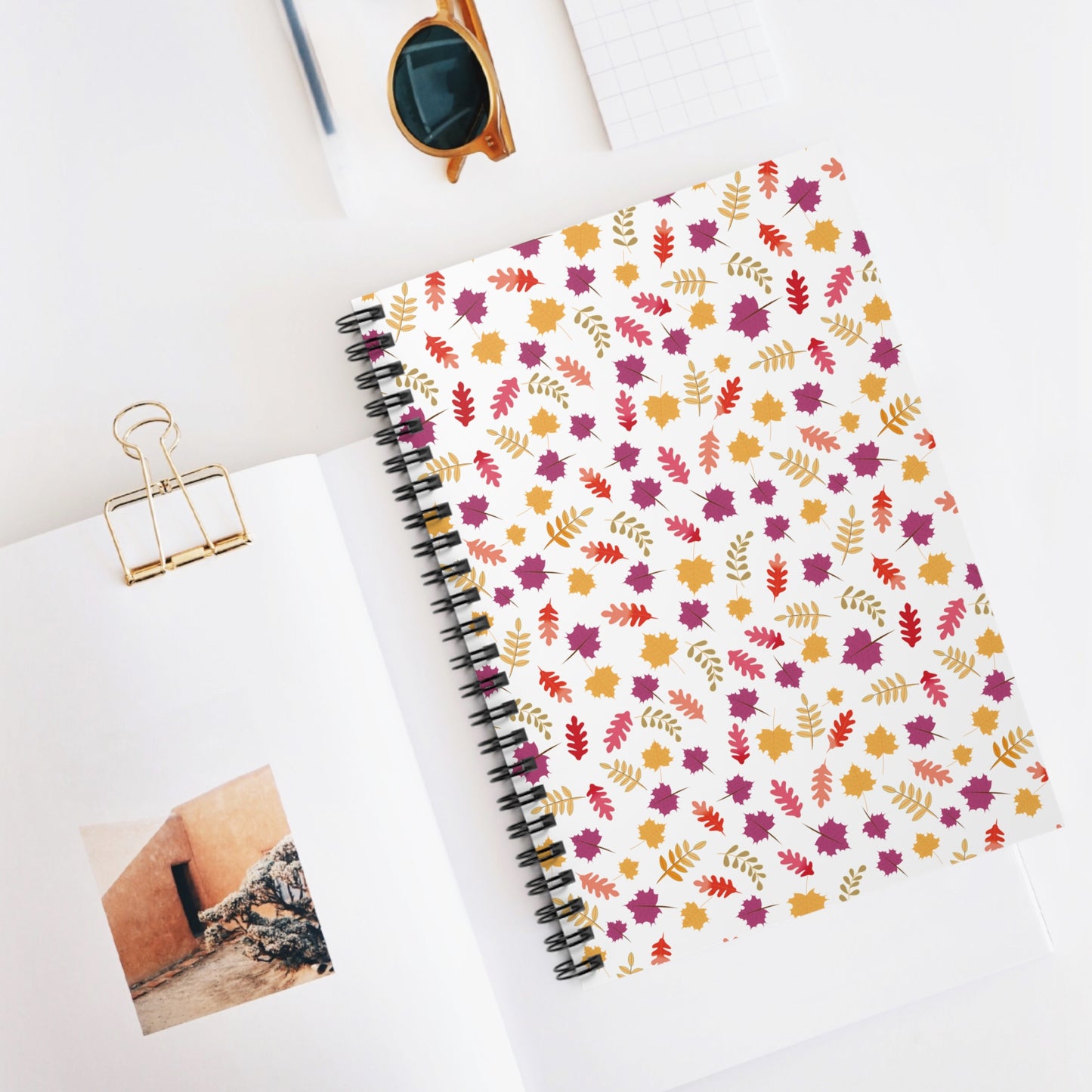Floral Spiral Notebook with autumn-inspired leaf pattern, showcased on a minimalist workspace. Ideal for creative note-taking, reflecting FireBrook Essentials' focus on stylish, joyful designs. Includes gold binder clip and sunglasses.