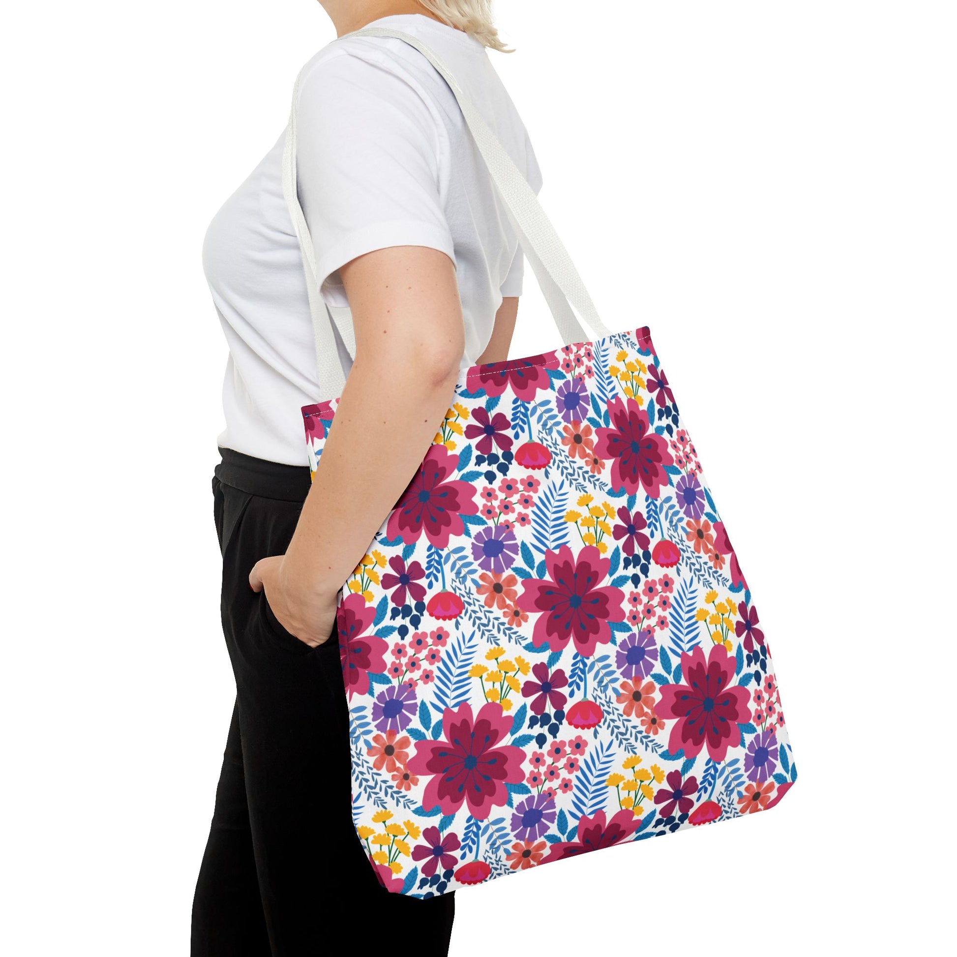 The Violet Daisy Carnival Tote Bag, with vibrant floral patterns, hangs on a shoulder. It's perfect for summer outings, embodying FireBrook Designs' joyful and stylish essence.