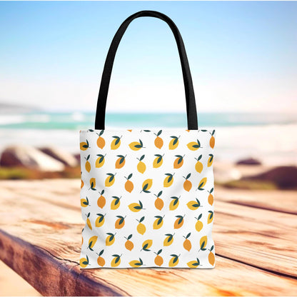 Lemon Drop Toss Tote Bag on wooden surface, showcasing a vibrant pattern of lemons with green leaves. Ideal for summer outings, this durable bag embodies FireBrook Designs' uplifting and joyful style.