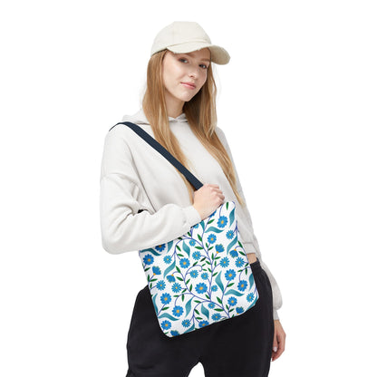 Blue Floral Tote Bag featuring a white base adorned with blue flowers and green leaves, worn over the shoulder by a model. Ideal for summer outings, reflecting FireBrook Essentials' vibrant, joyful design ethos.