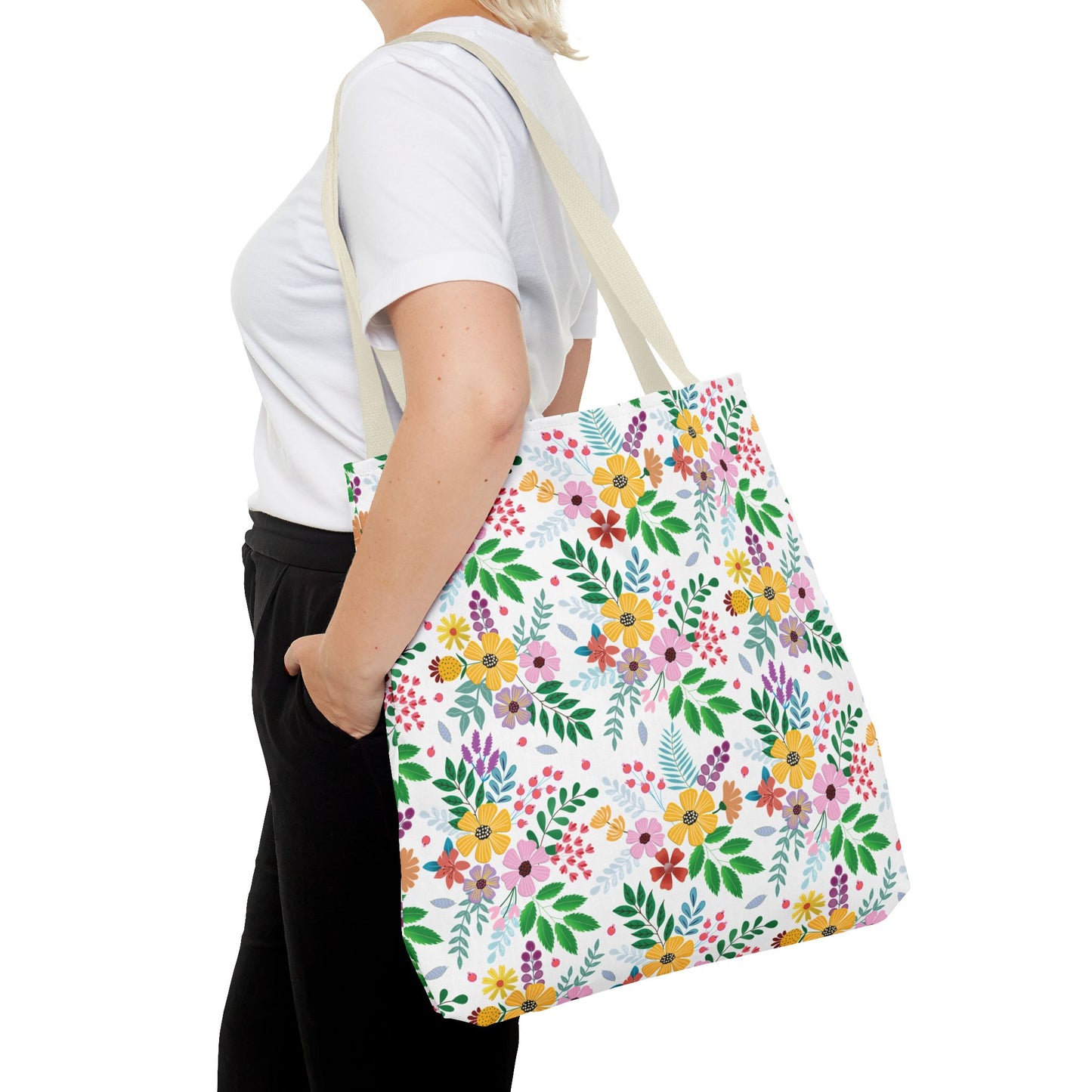Person carries a Floral Tote Bag with a vibrant flower pattern, ideal for summer outings. The large white canvas bag complements the casual white T-shirt and black pants ensemble, embodying FireBrook Essentials' joyful style.