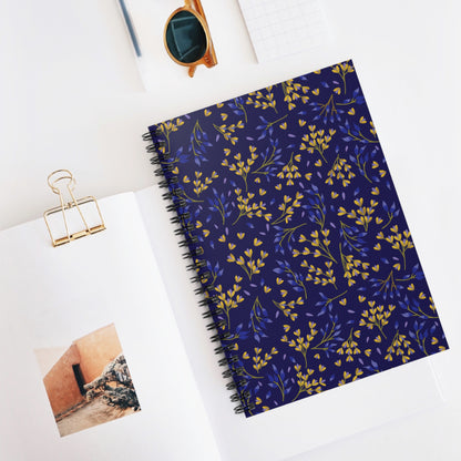 Floral Spiral Notebook with navy cover adorned with yellow and blue floral sprigs, ideal for creativity and organization. Features sleek metal spiral binding, shown with a magazine and amber sunglasses for a stylish touch.