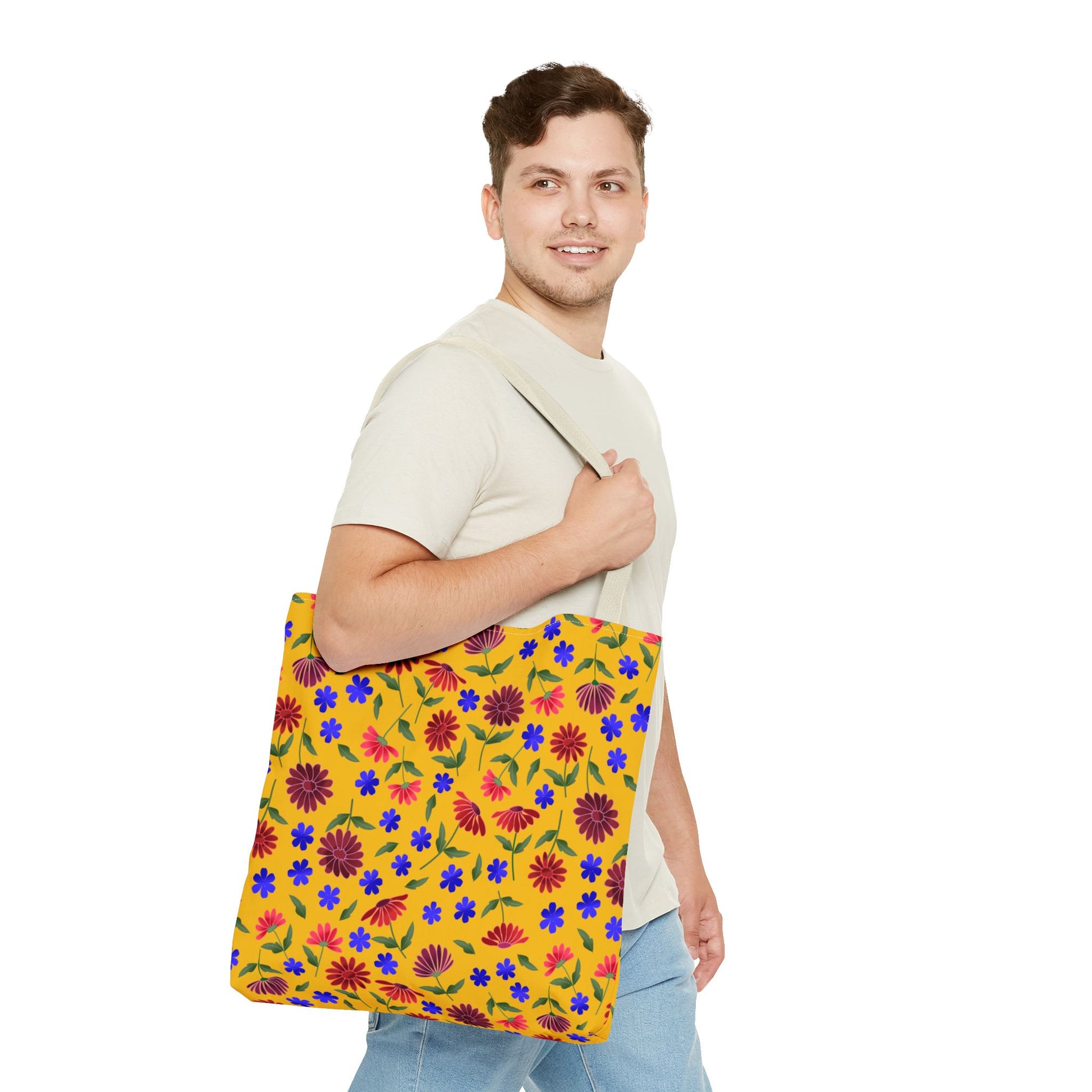 A young man wears the Golden Wildflower Tote Bag, showcasing its vibrant floral design with red, purple, and blue flowers. The bag's sturdy black straps complement its cheerful, practical style, embodying FireBrook Essentials' uplifting spirit.