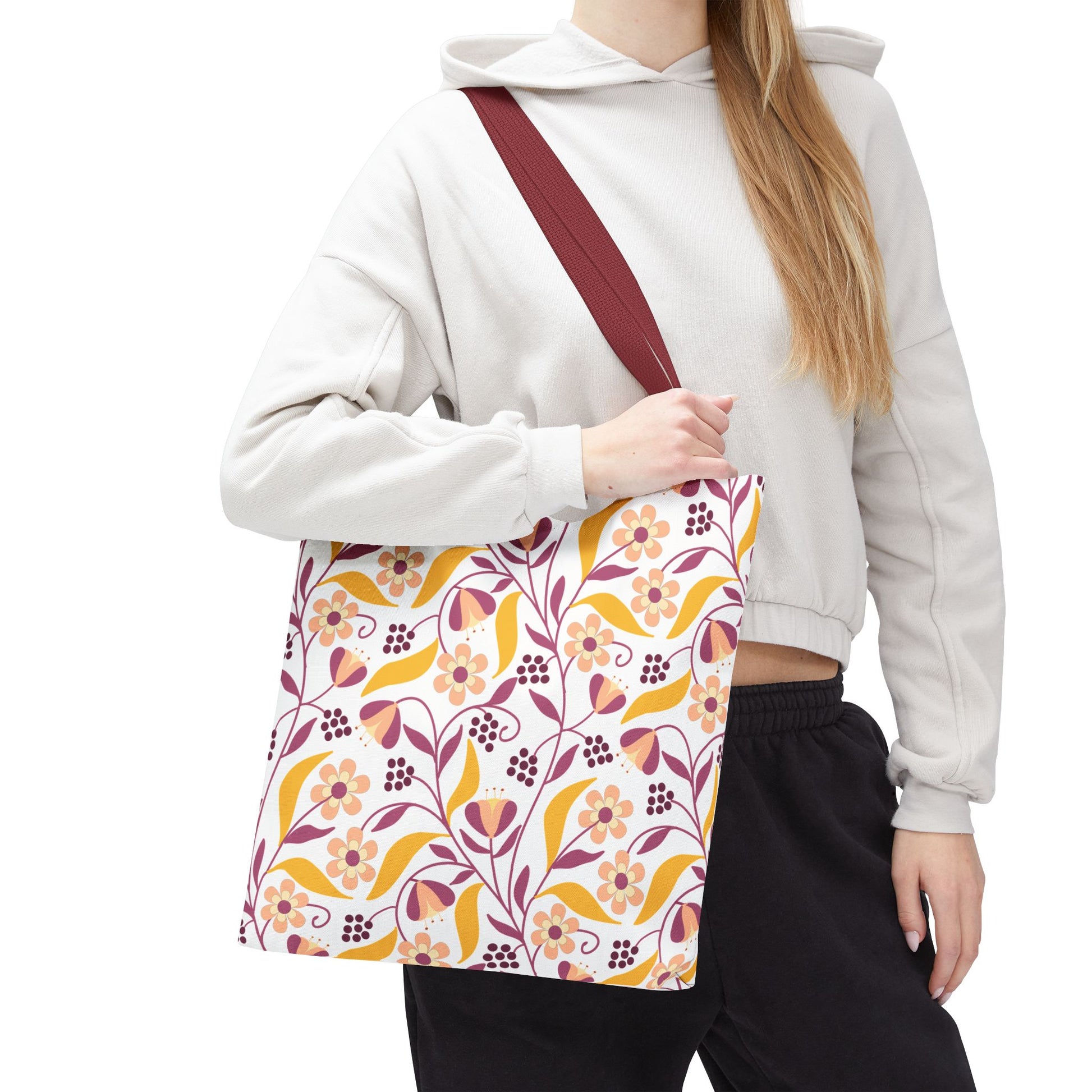 Golden Paisley Floral Tote Bag with mustard, dusty rose, and burgundy floral pattern, held by a solid burgundy strap, ideal for summer outings. Worn with a light hoodie and dark pants.