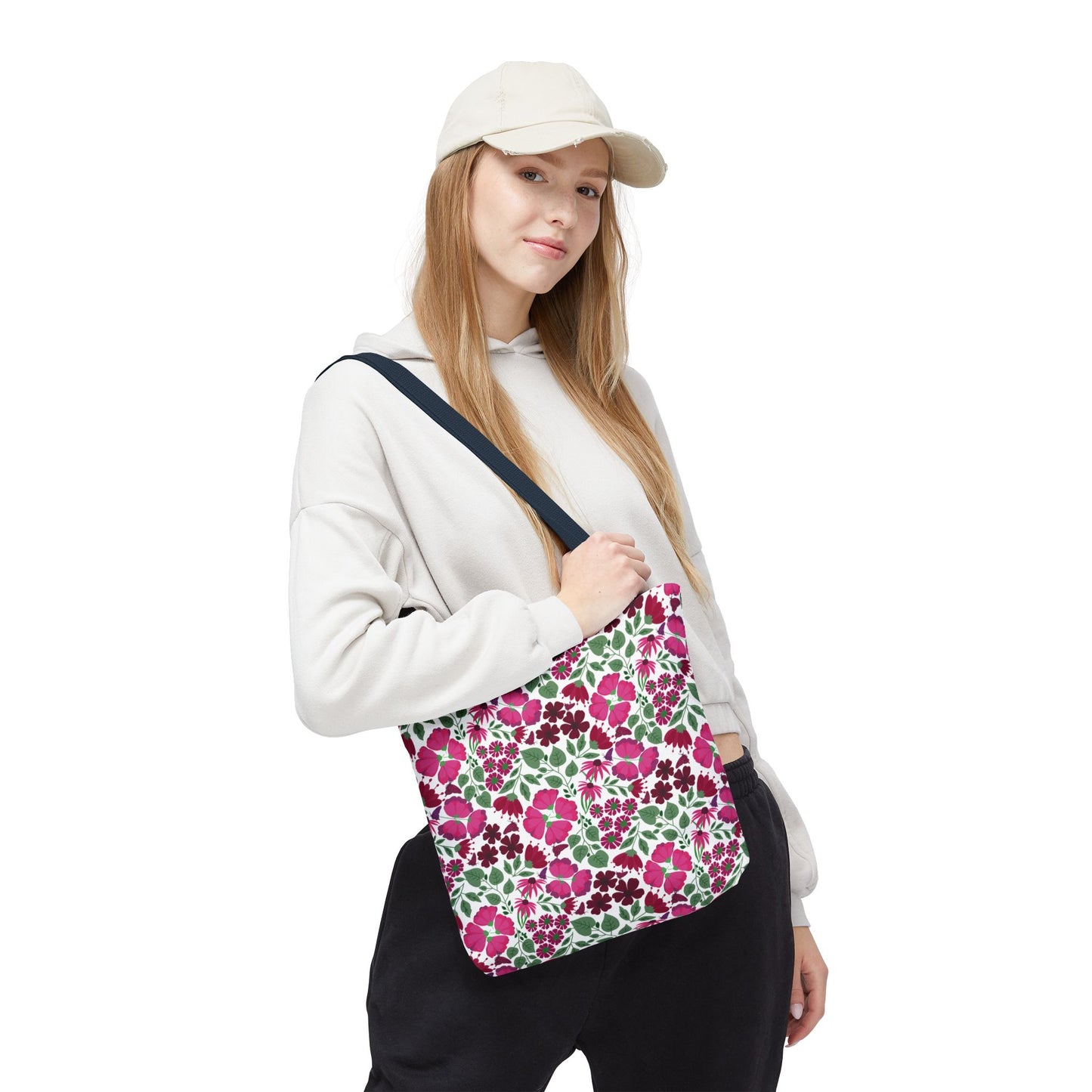 Young woman wearing a light hoodie and beige cap carries the Pink Lady Tote Bag. The bag showcases vibrant pink and burgundy floral designs, adding a cheerful touch to her casual outfit.