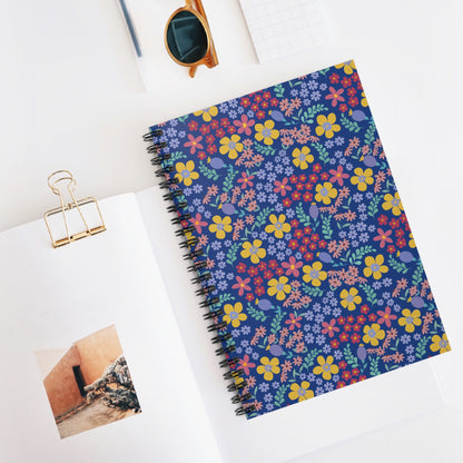 Floral Spiral Notebook with vibrant blooms on the cover, atop an open book. Features include durable spiral binding and compact size, perfect for jotting notes or sketching ideas.