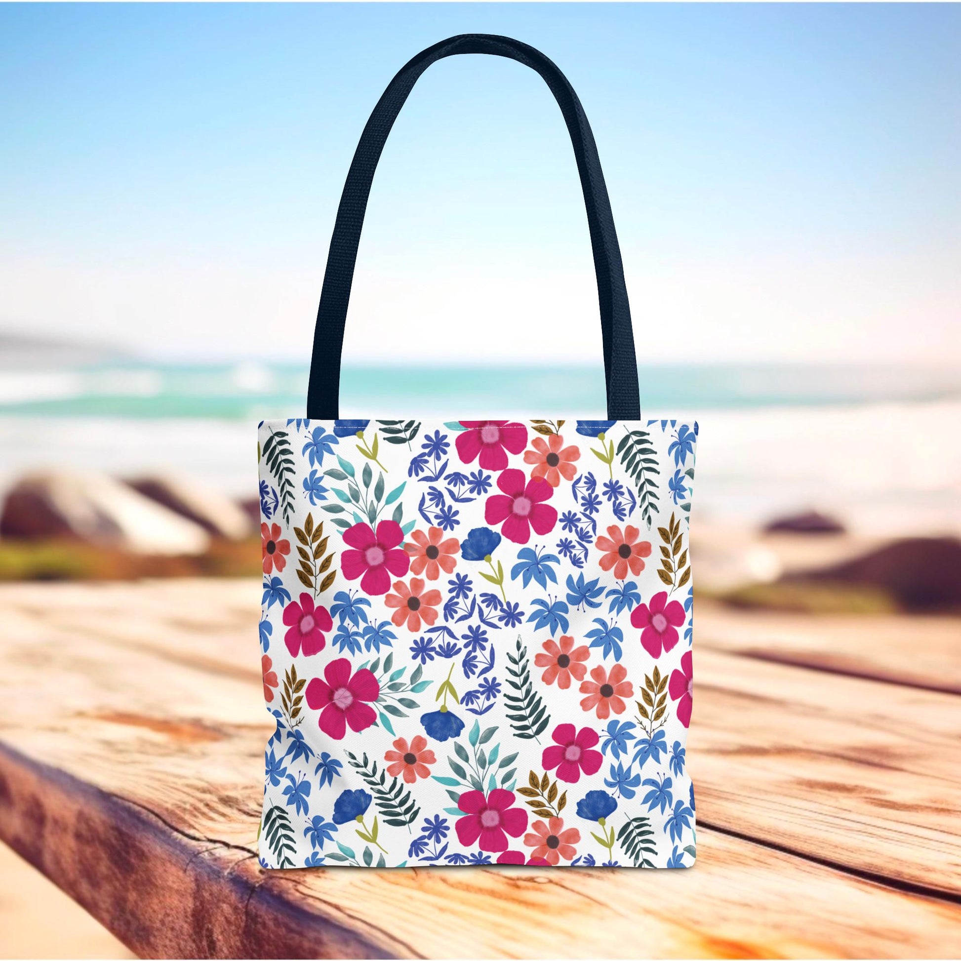 Floral Tote Bag with colorful blossoms and navy handles stands on a wooden surface, ideal for summer adventures. Perfect for those seeking vibrant, joyful designs from FireBrook Essentials.