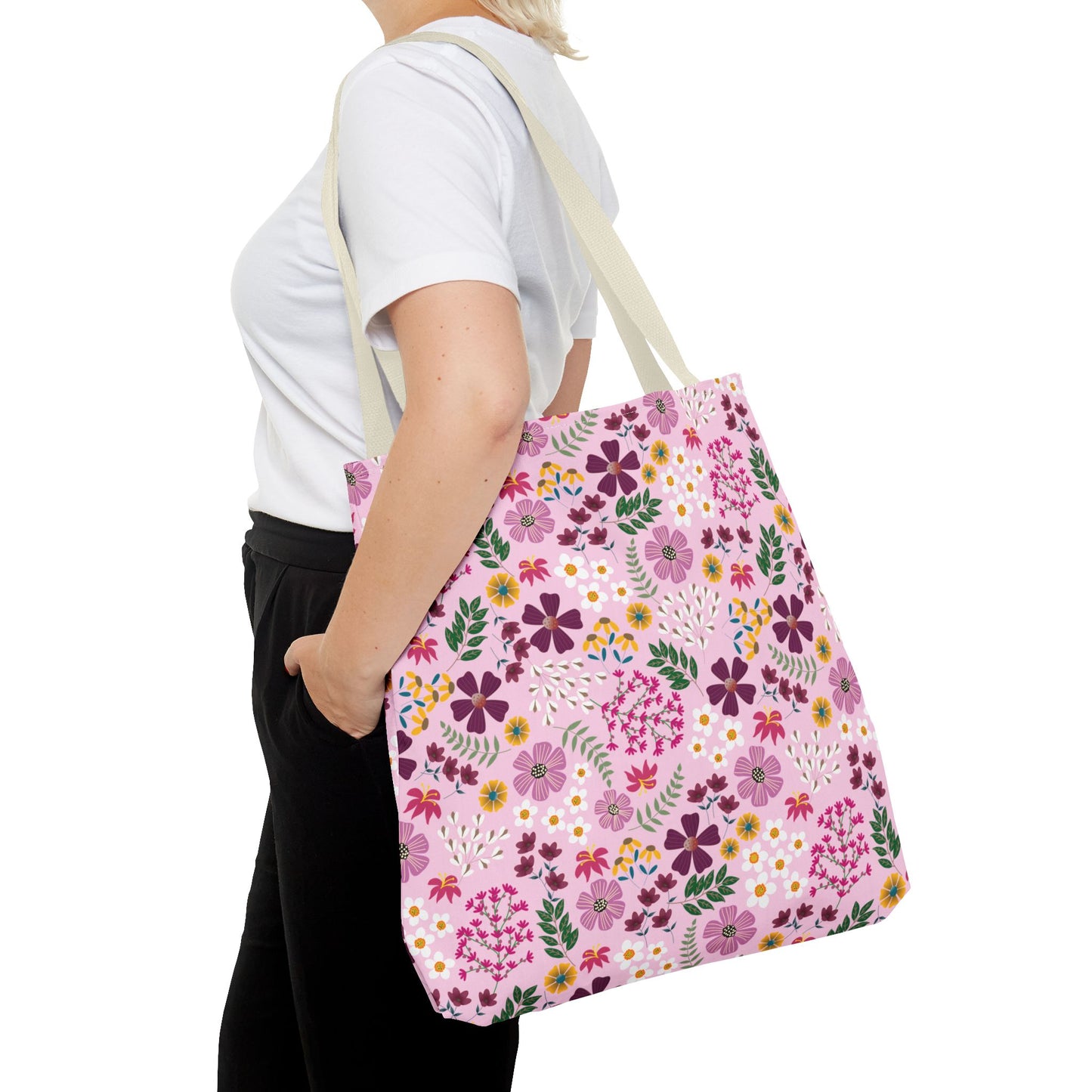 The Rose Garden Blush Tote Bag features a vibrant floral print on a pink background, carried over the shoulder by a person wearing a white T-shirt, embodying FireBrook Essentials' uplifting design ethos.