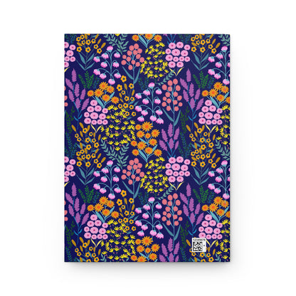 HARDCOVER JOURNAL, MATTE, RULED, 5X7, SEWN BIND, CLEAN-TEAR PAGES - FLORAL MEADOWS, BLUE BACKGROUND featuring vibrant floral patterns with pink, coral, and orange flowers on navy-blue. Subtle white barcode in corner.