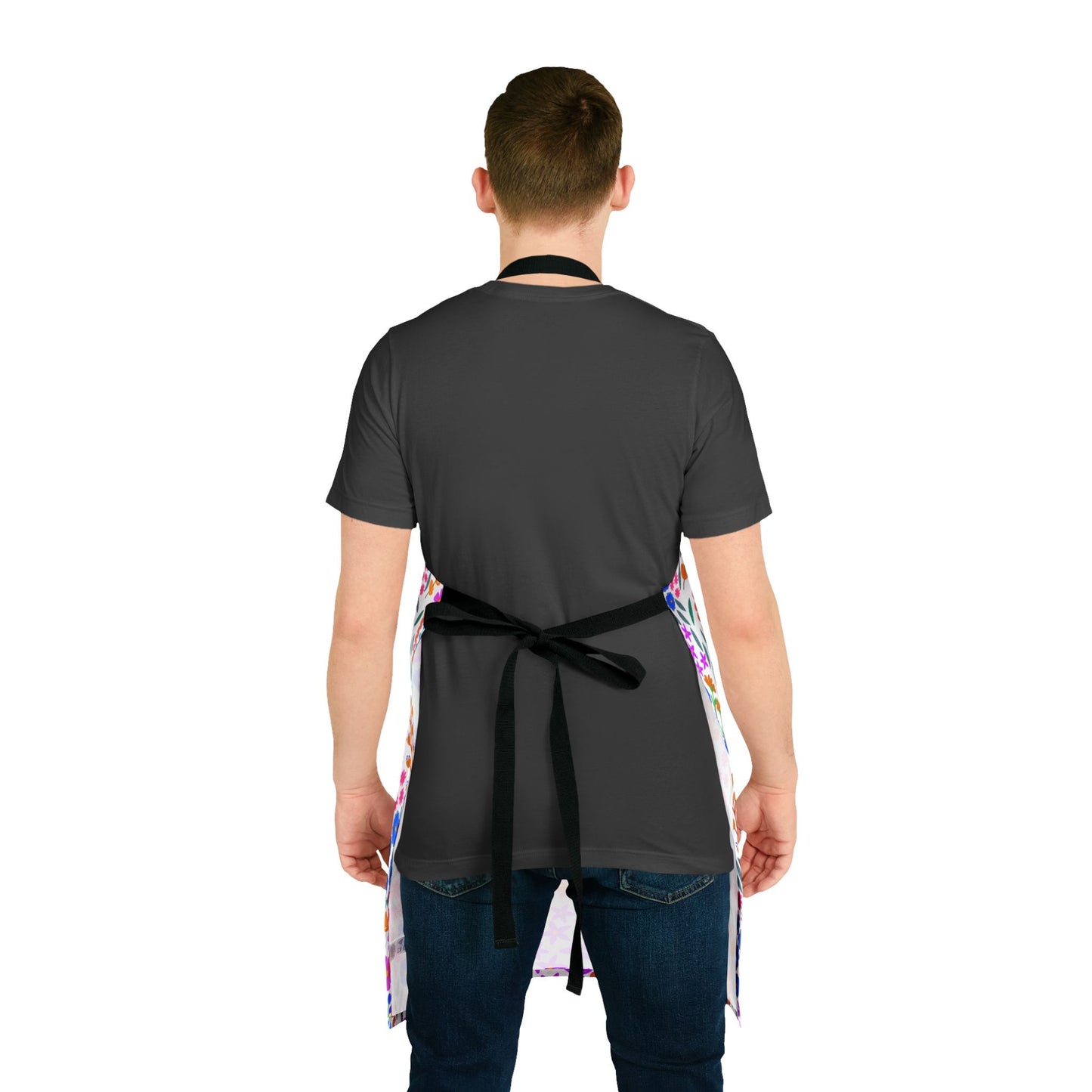 A person wears a Floral Apron with vibrant splatter patterns over a dark gray T-shirt and blue jeans, showcasing its stylish, stain-free design from FireBrook Essentials.