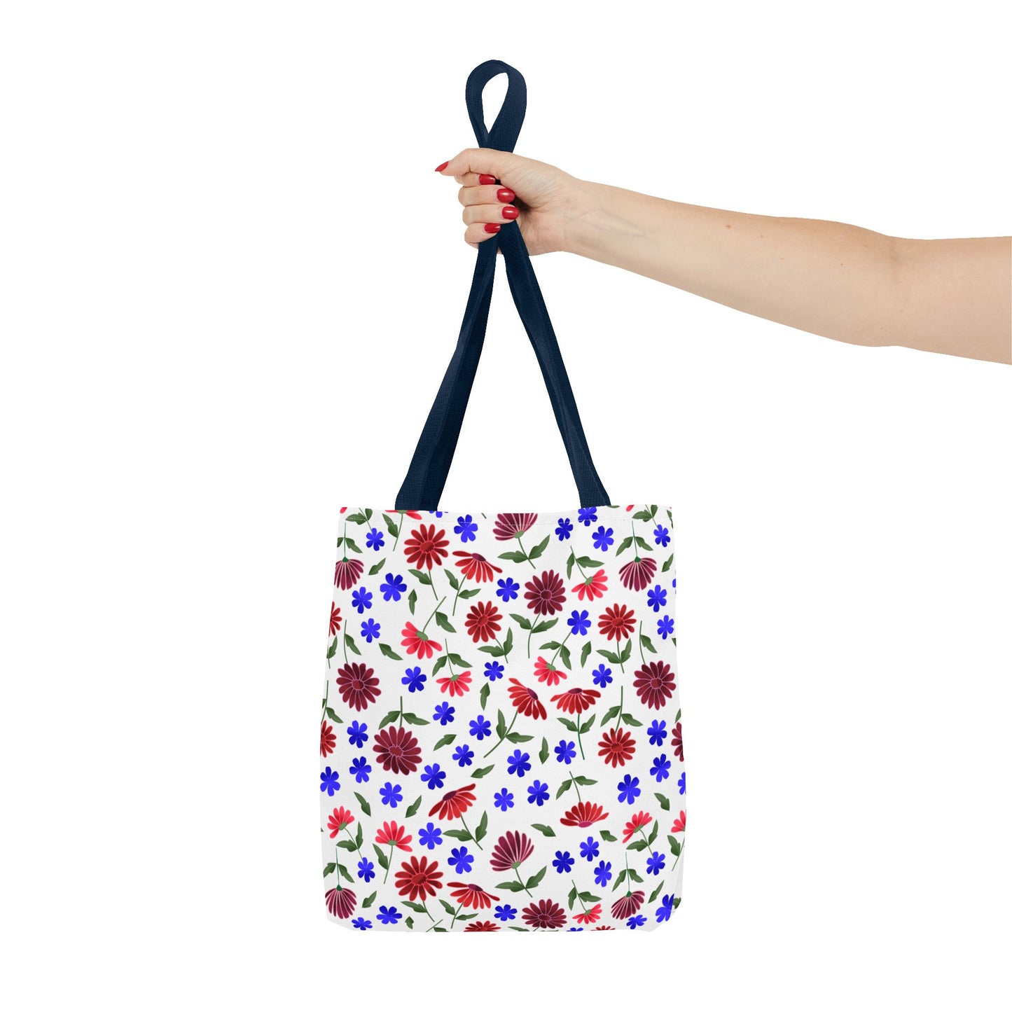 Floral Pattern Tote Bag — Red & Blue Wildflower All-Over Print held by a hand with red nails, showcasing its white canvas body adorned with vibrant floral patterns and navy handles, embodying cheerful, practical elegance.