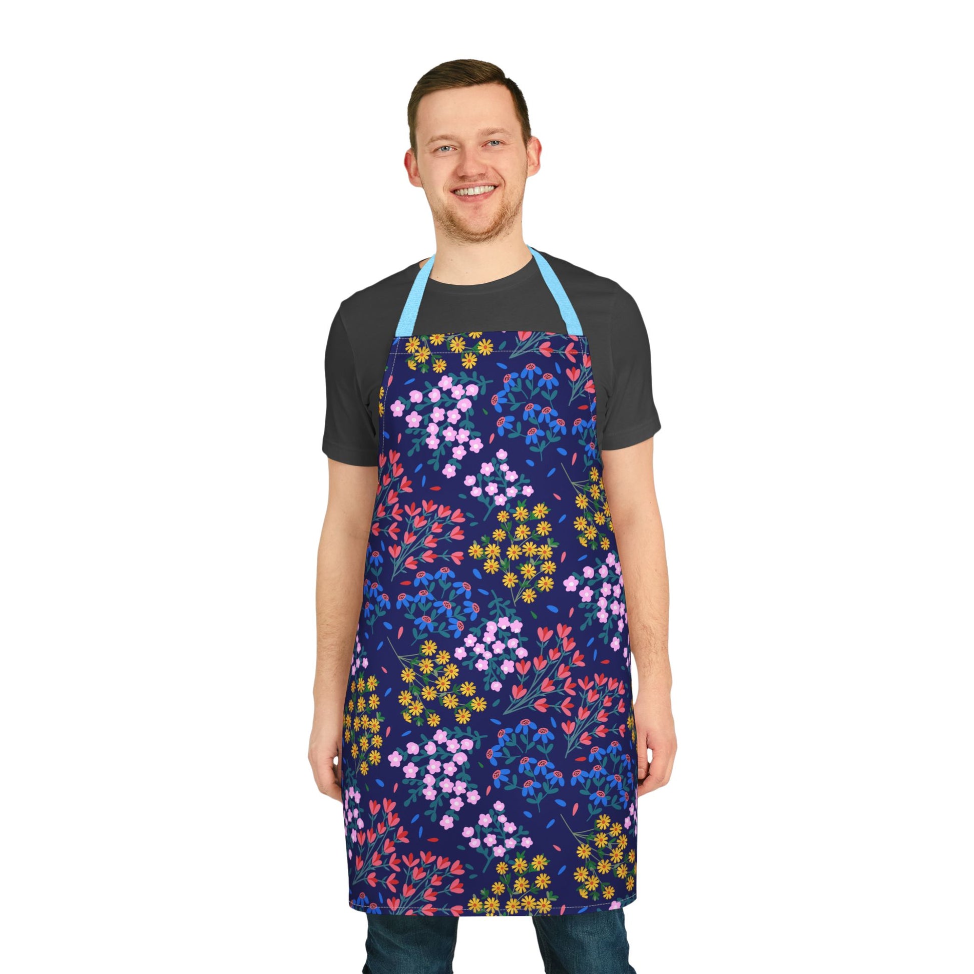 Smiling man models the Floral Apron by FireBrook Designs, showcasing vibrant flower patterns on a navy background, highlighting its stylish, stain-free design for baking, cooking, or crafting.