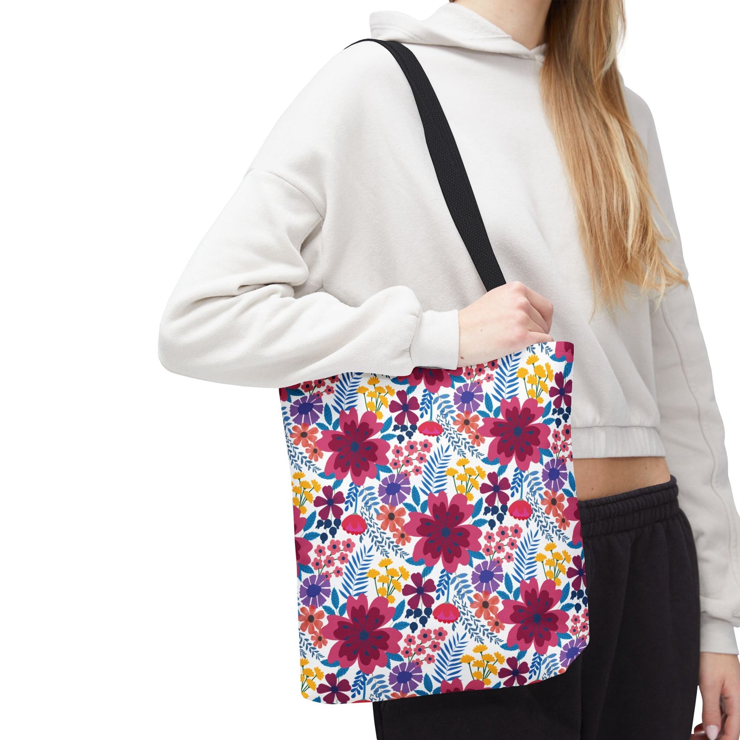 A person carries the Floral Tote Bag from FireBrook Designs, showcasing its vibrant multicolored floral pattern, perfect for summer outings. The light-gray cropped hoodie complements the tote's cheerful design.