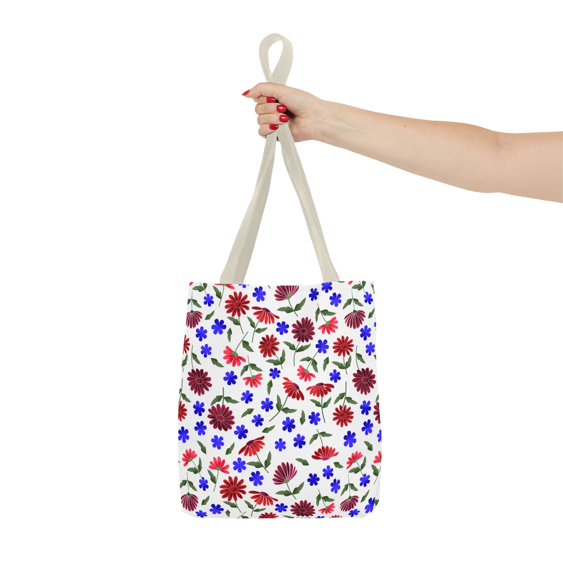 Floral Pattern Tote Bag — Red & Blue Wildflower All-Over Print held by a person with red nails. Showcases vibrant floral design with green leaves, black handles, and roomy corners, embodying FireBrook Essentials' joyful style.