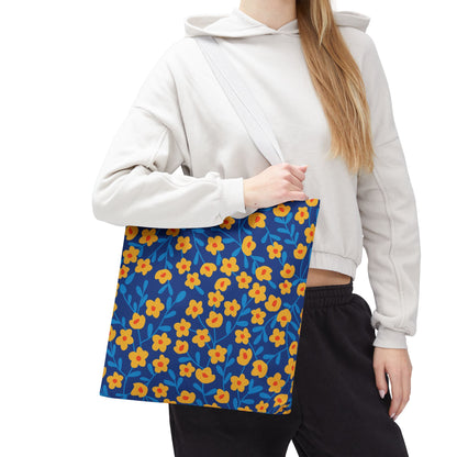 Cobalt Poppy Field Tote Bag features a dark blue background with stylized yellow-orange flowers and light blue leaves, carried over the shoulder by a person wearing a light-colored hoodie.