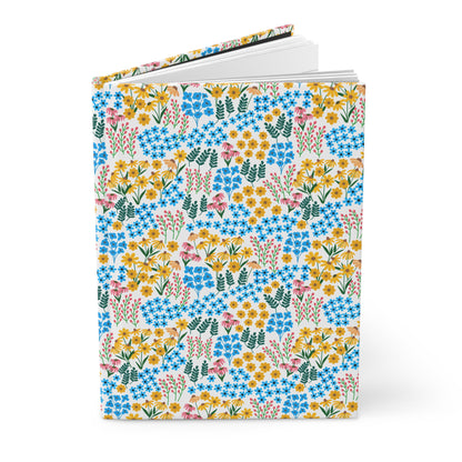 HARDCOVER JOURNAL, MATTE, RULED, 5X7, SEWN BIND, CLEAN-TEAR PAGES – WILDFLOWER MEADOW MIX features a ditsy-floral cover with blue, yellow, and pink blossoms, green sprigs, and blank lined pages inside.