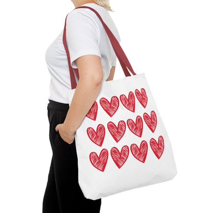 Hearts Tote Bag: A white tote adorned with red hearts, held by a person, showcasing its playful and charming design. Ideal for adding a touch of love to everyday outfits.