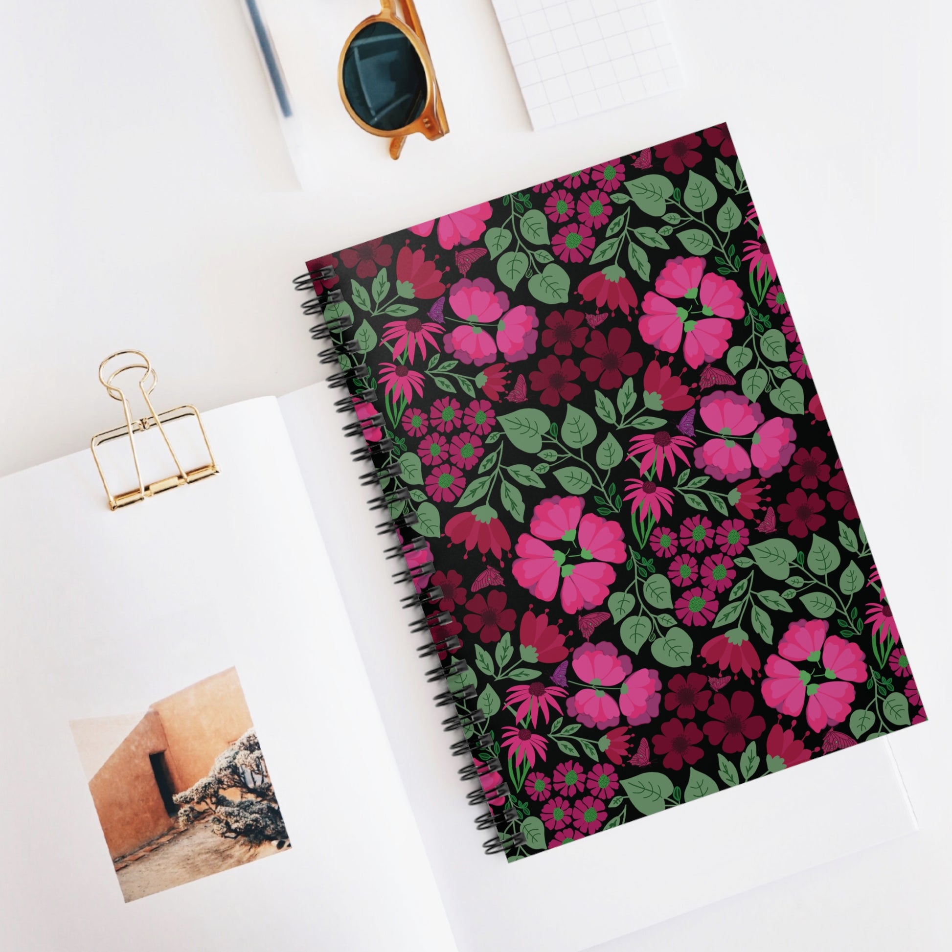 Floral Spiral Notebook with vibrant flowers and green leaves on a black cover, accompanied by round sunglasses and open book page, embodying FireBrook Designs' joyful, uplifting style.
