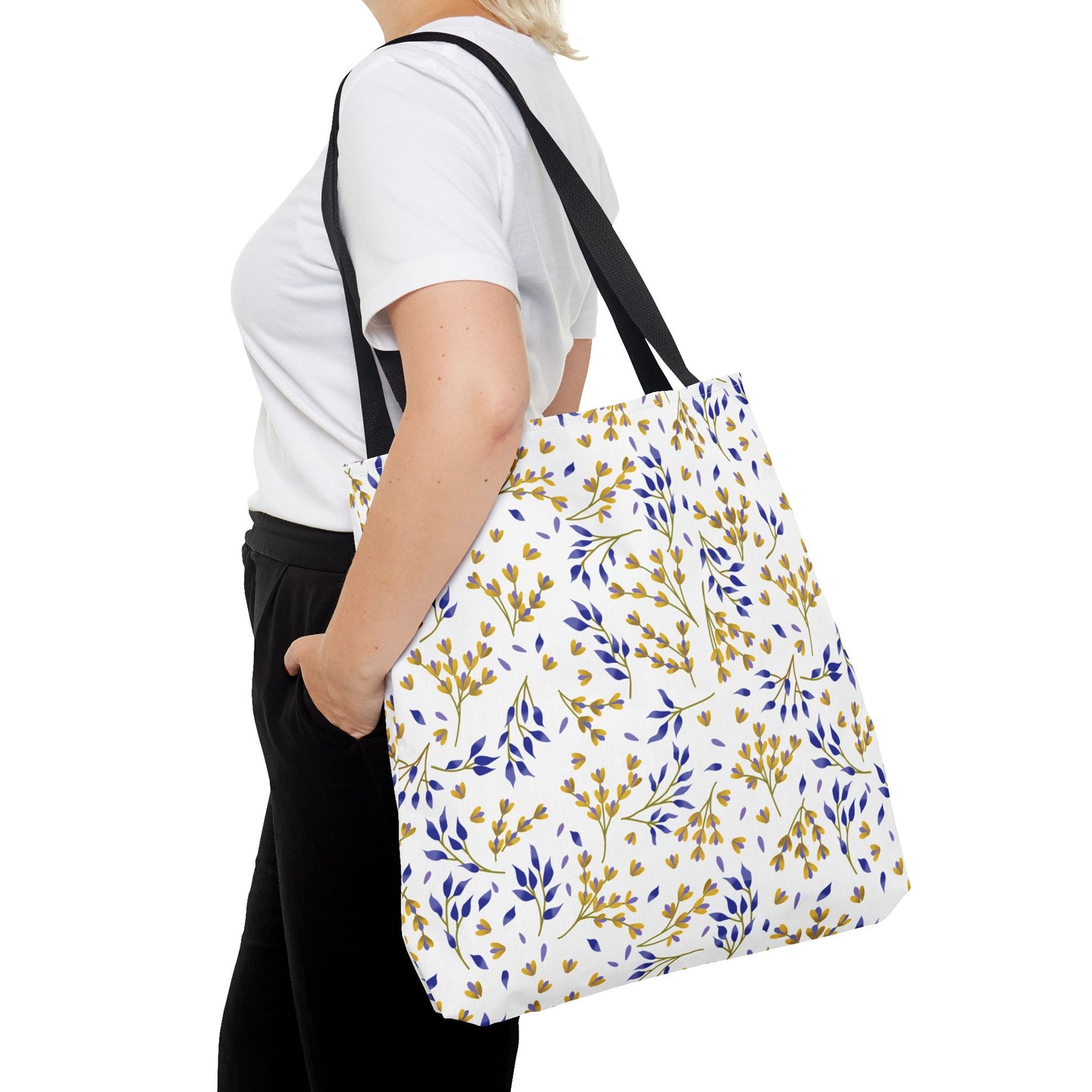Person wearing a plain white T-shirt carries a Floral Tote Bag with black straps, featuring a cheerful botanical print of yellow and blue leaves, ideal for summer outings.